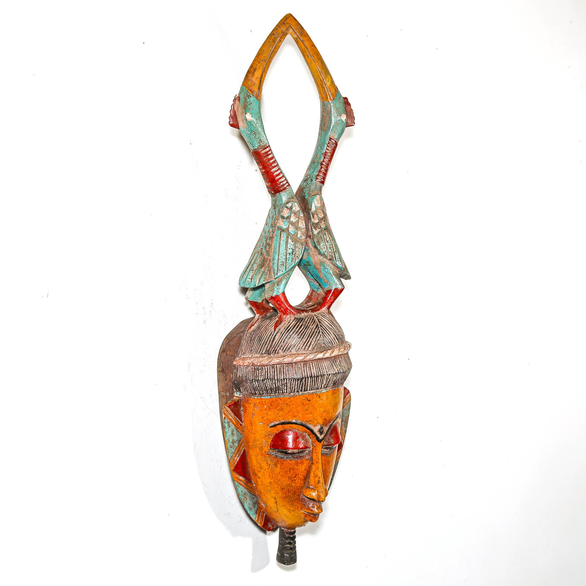 Colorful wooden african mask with intricate bird sculptures on a white wall
