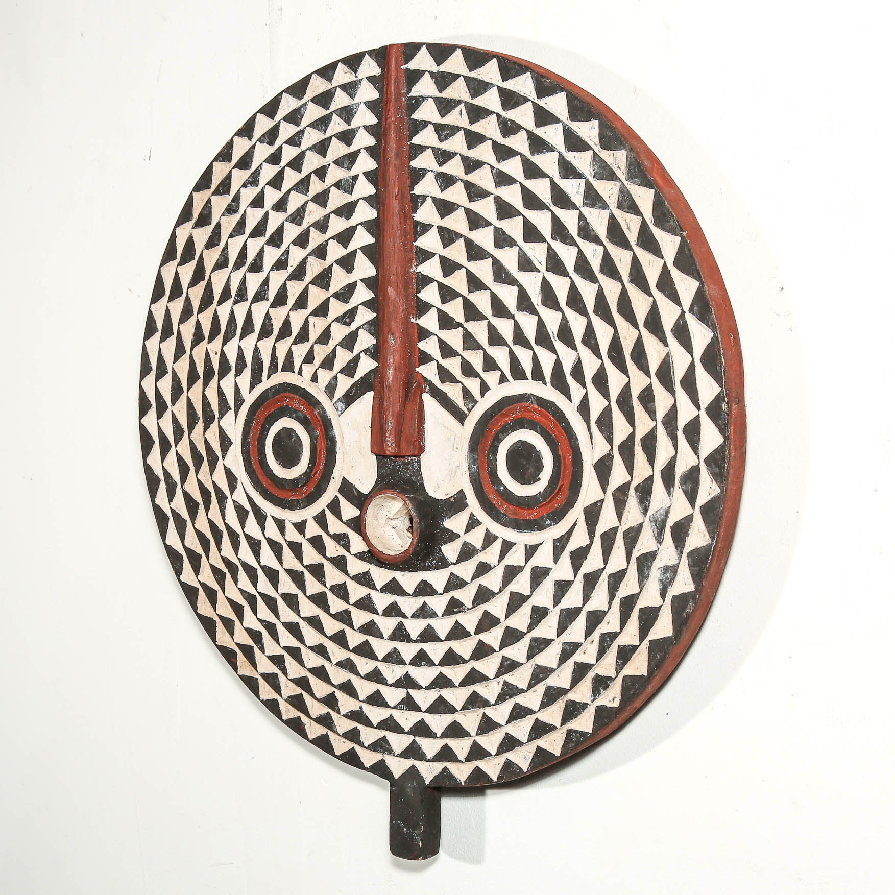 Decorative round tribal art with a face and geometric patterns on a white background