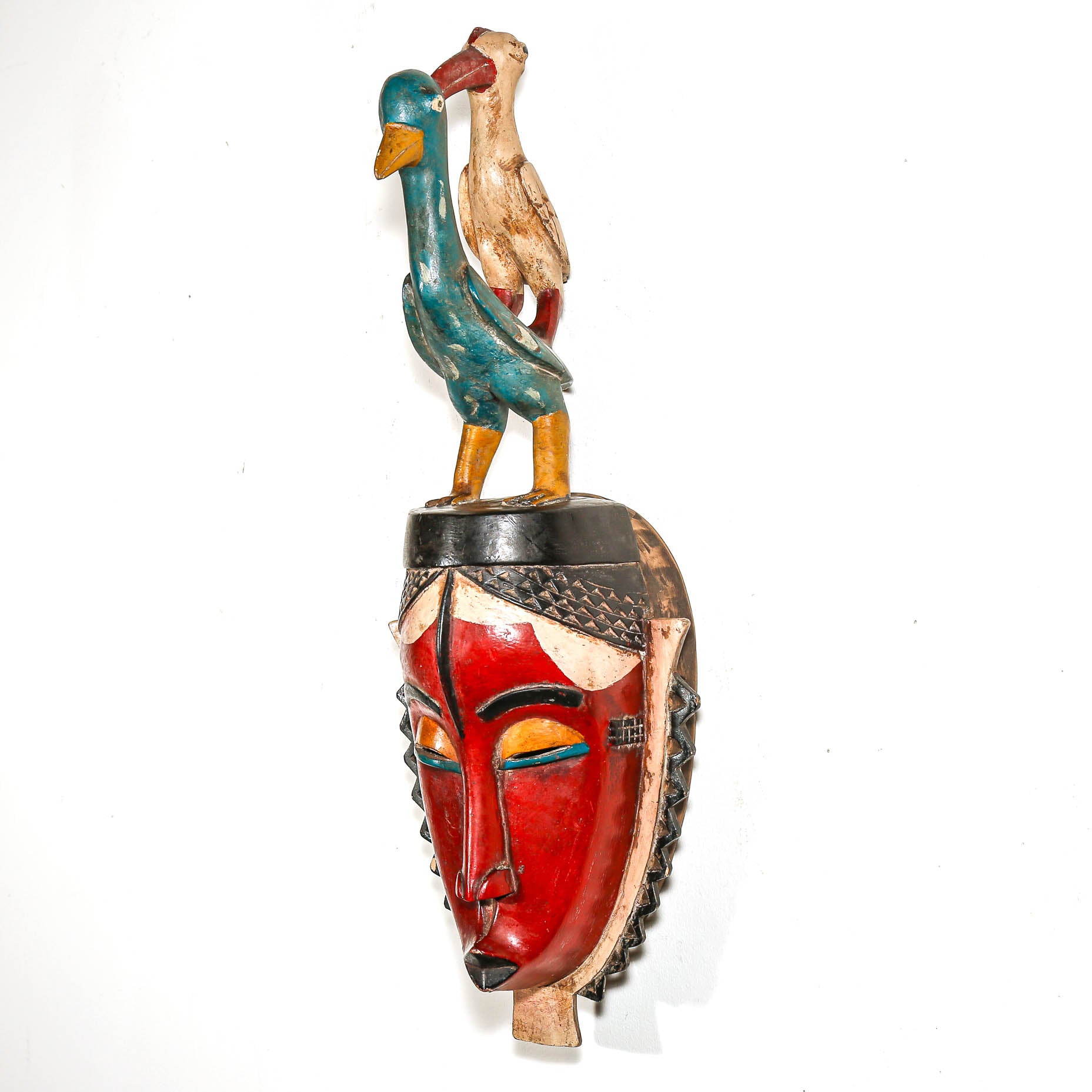 Decorative mask with two birds on top against a white bedroom wall