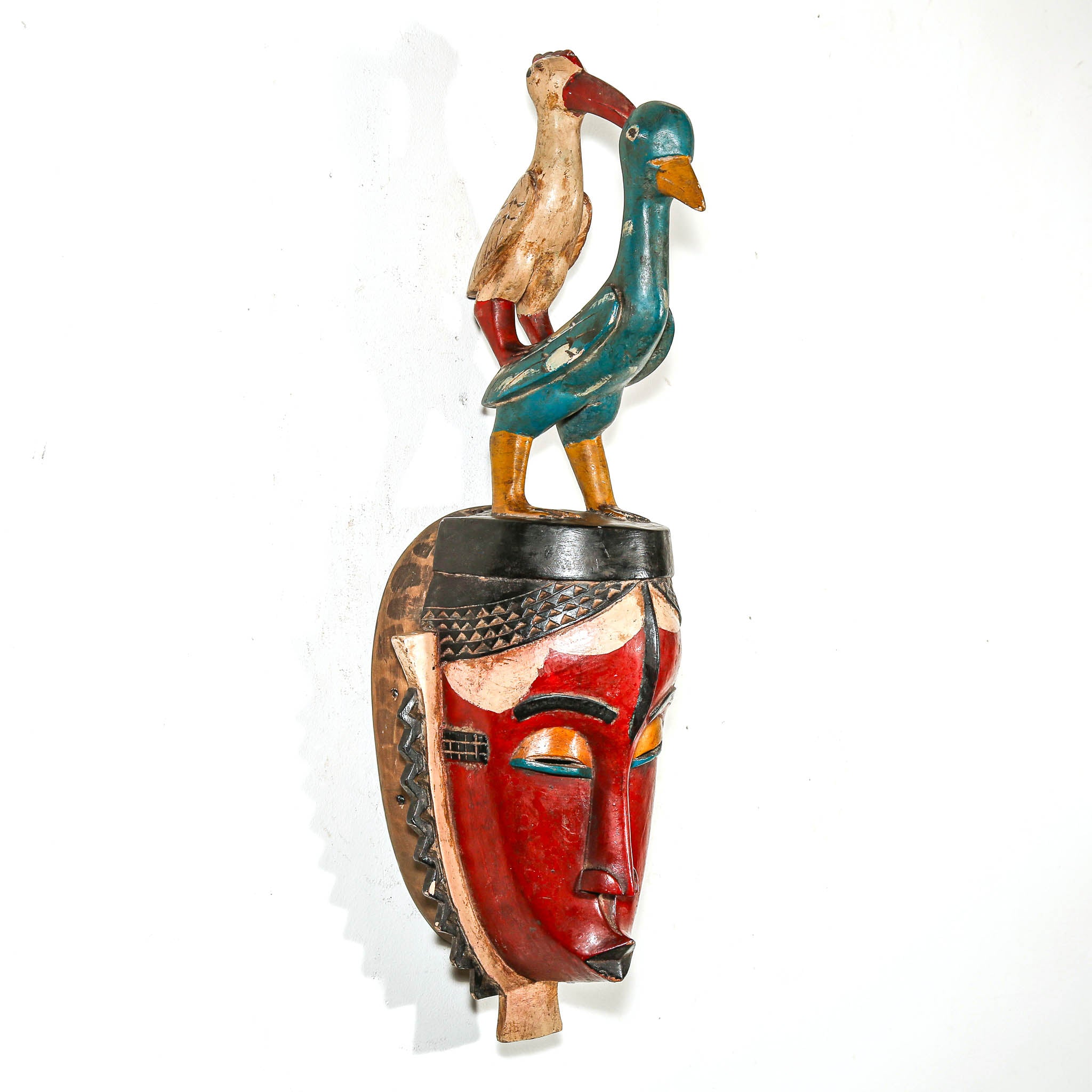 Decorative wall art with a colorful face design and bird figures on a white background