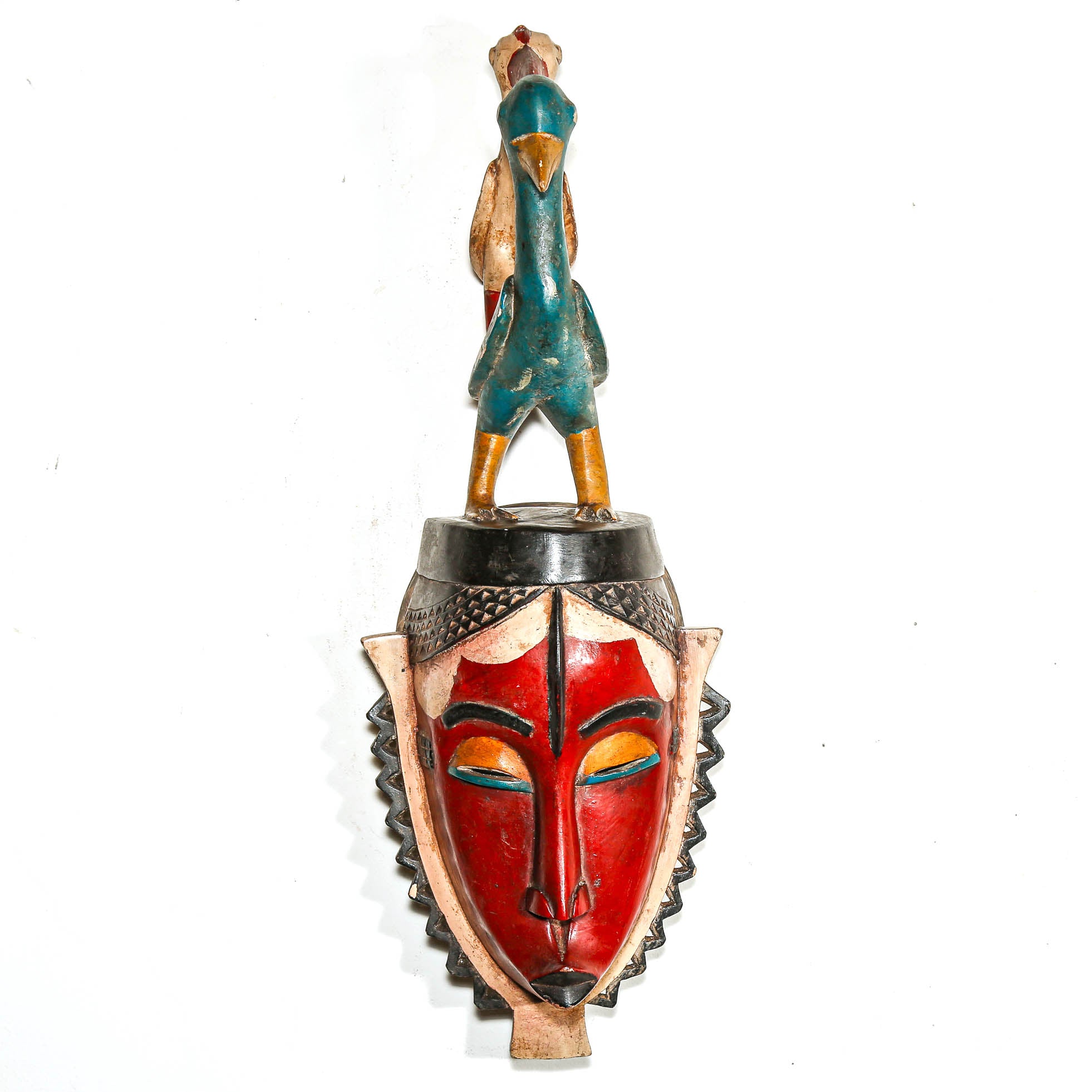 Decorative mask with a red face and green and brown accents on a white background