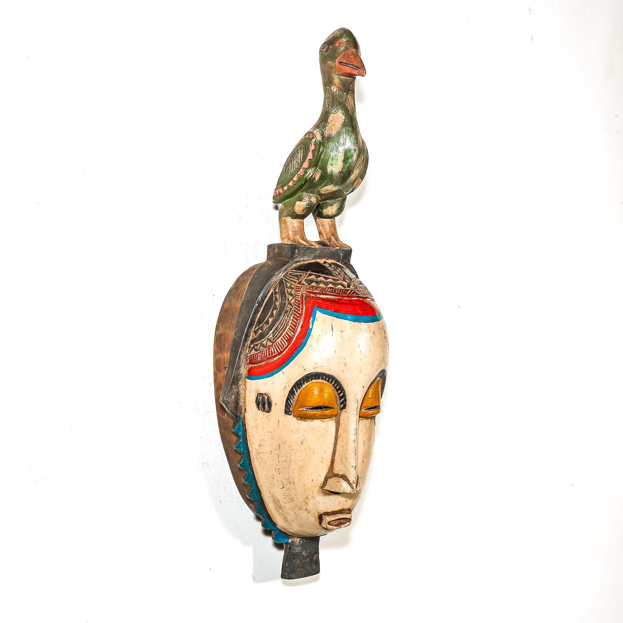 Decorative object with a face design and a bird figure on top against a white background from Africa