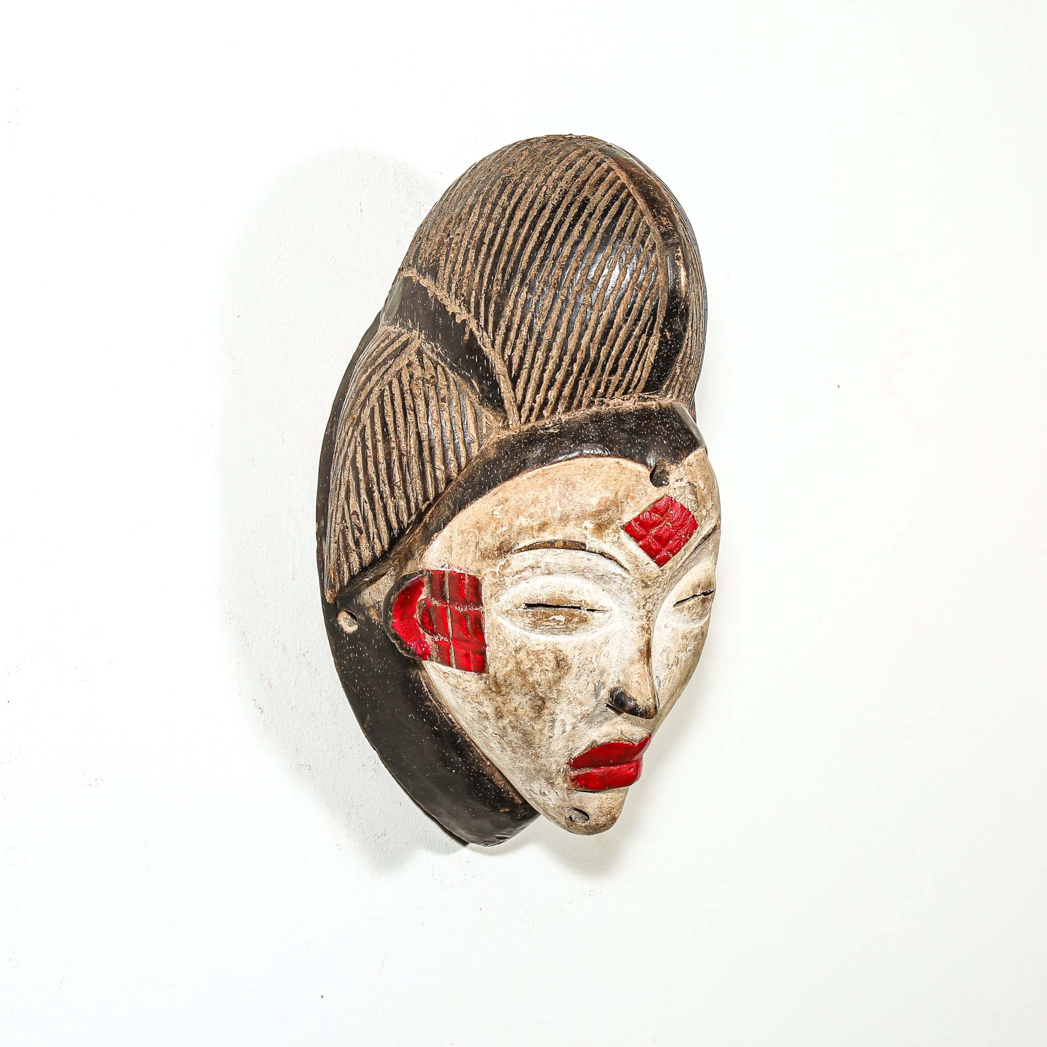 Decorative mask with black hair, red accents, and a white face on a white background
