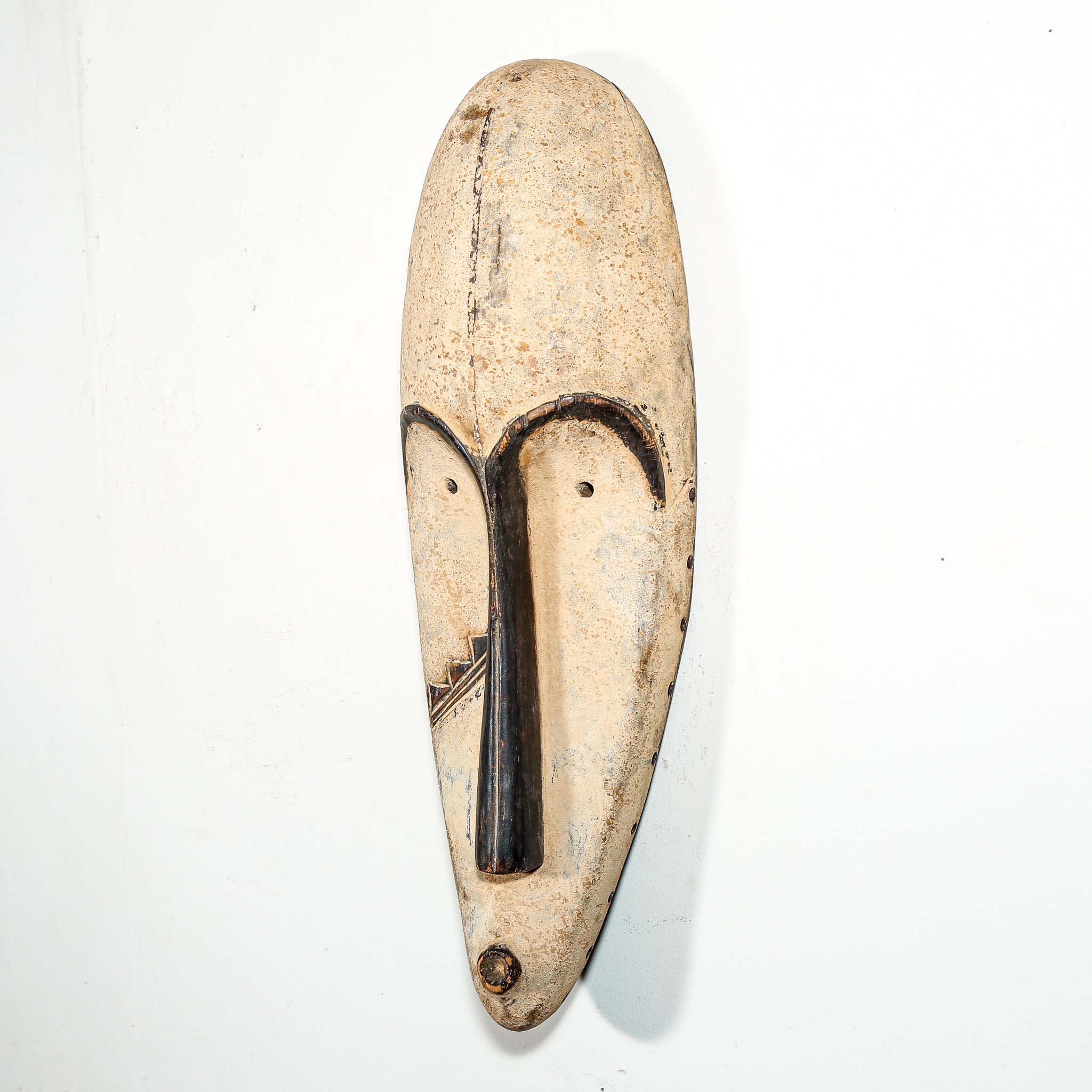 Authentic African mask to purchase online with black and white designs hanging on a white wall
