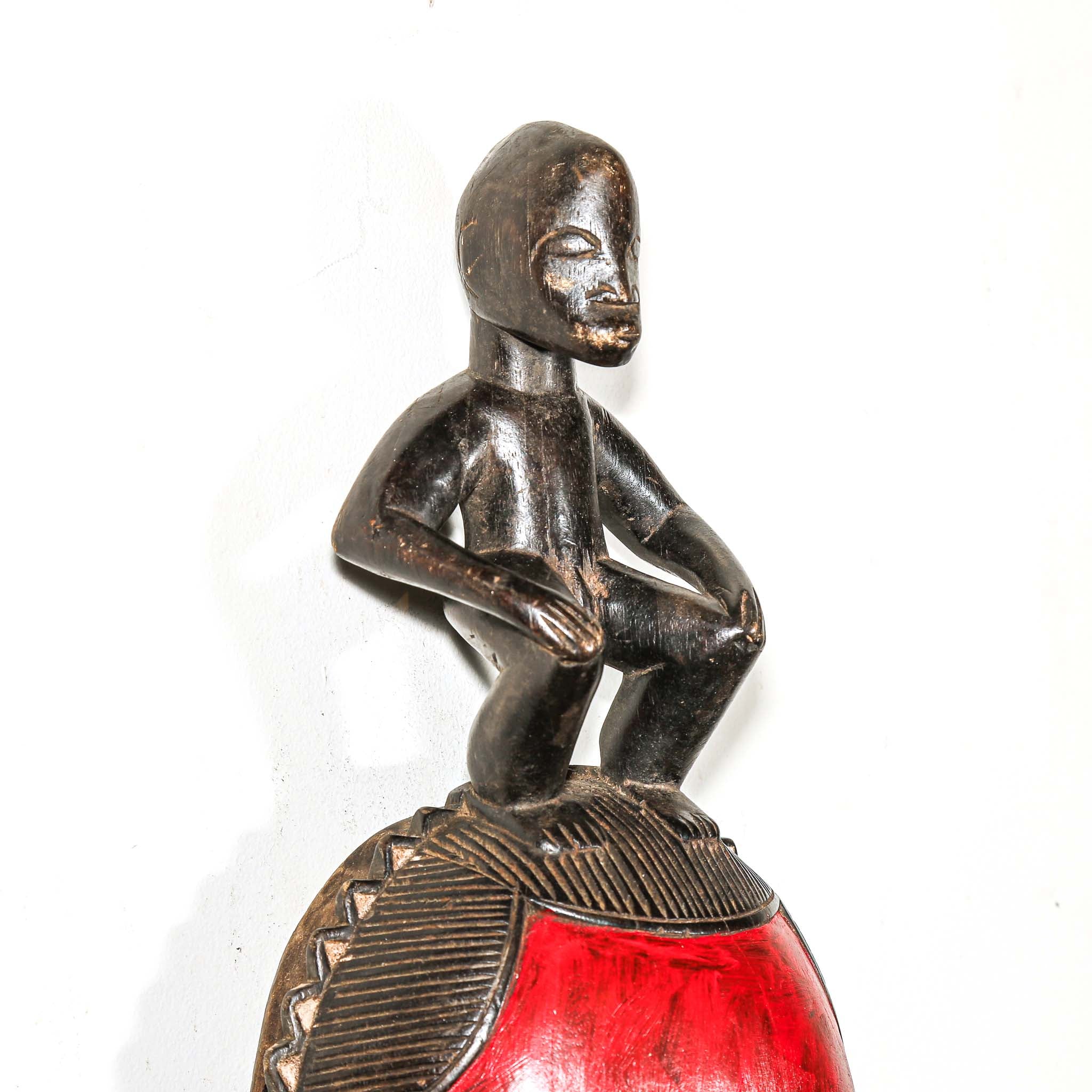 African mask with a red face and a figure on top against a white background