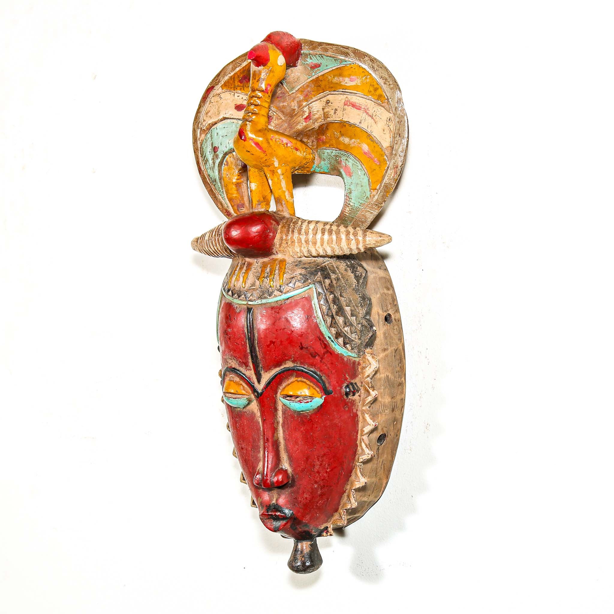African mask with a red face and a figure on top against a white background
