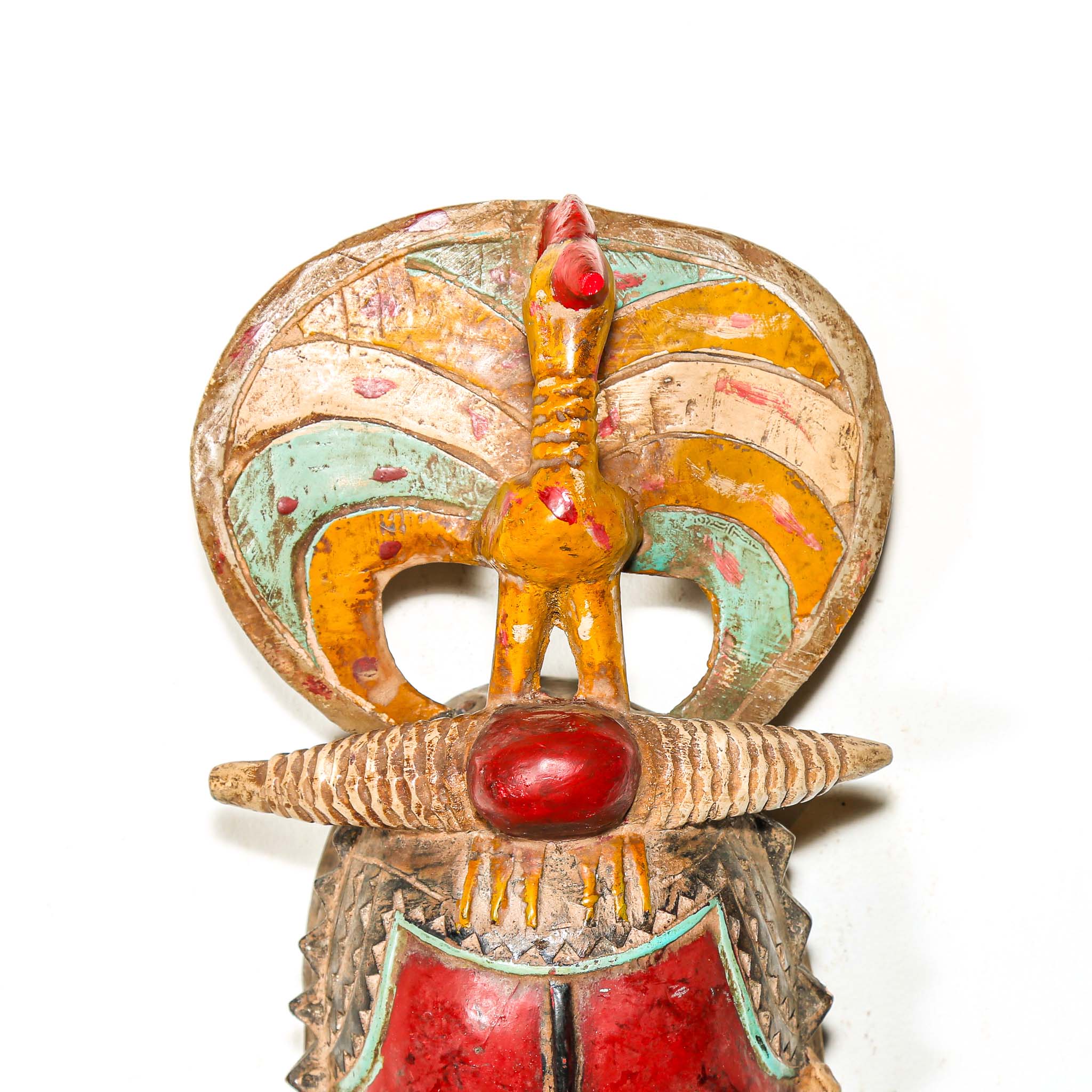 African mask with a red face and a figure on top against a white background