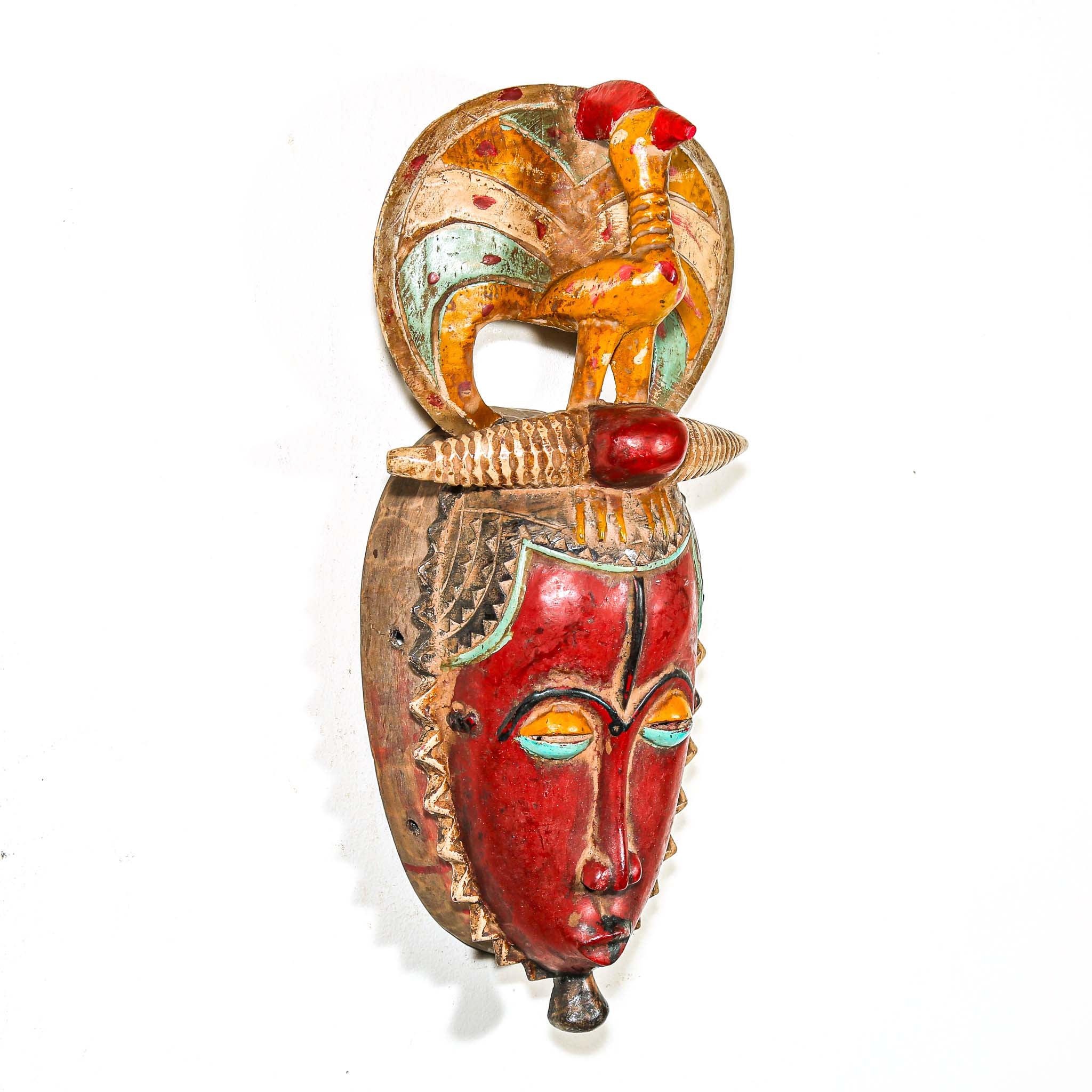 African mask with a red face and a figure on top against a white background