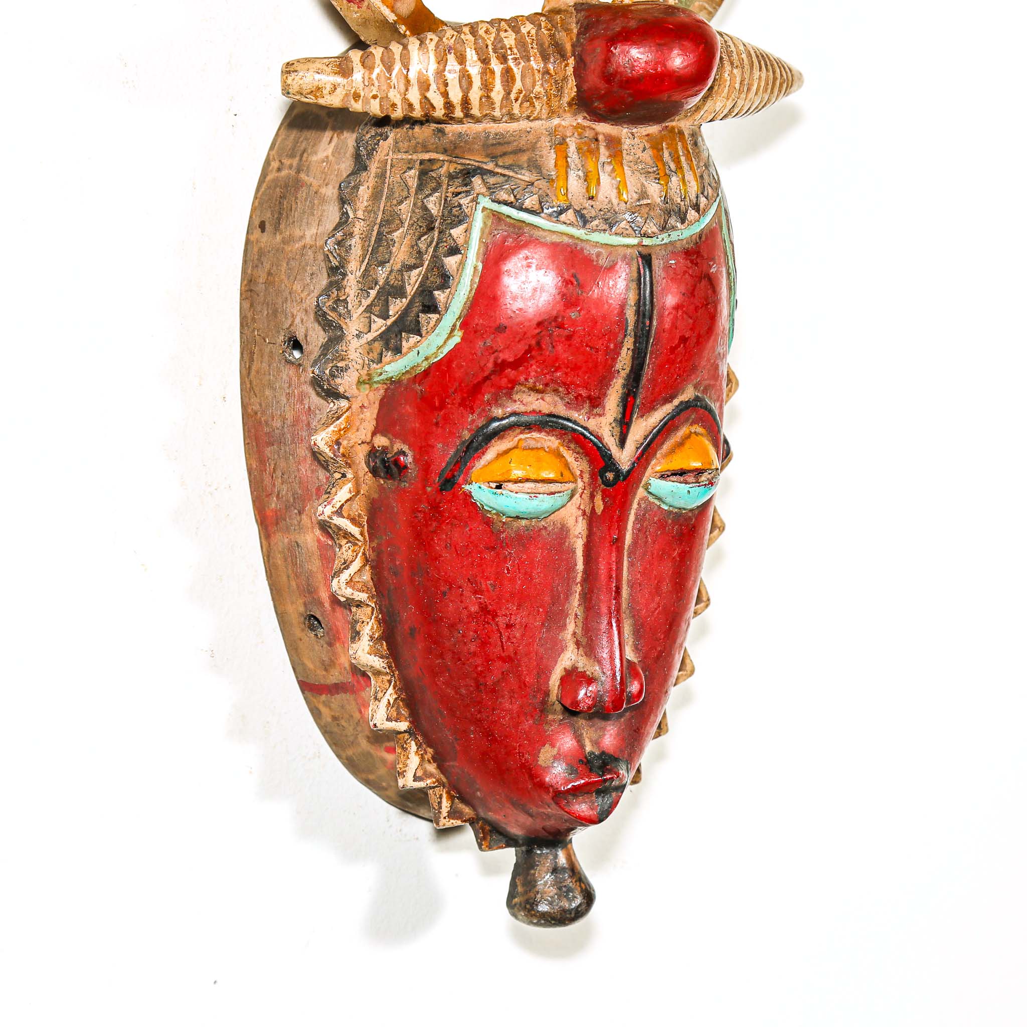 African mask with a red face and a figure on top against a white background