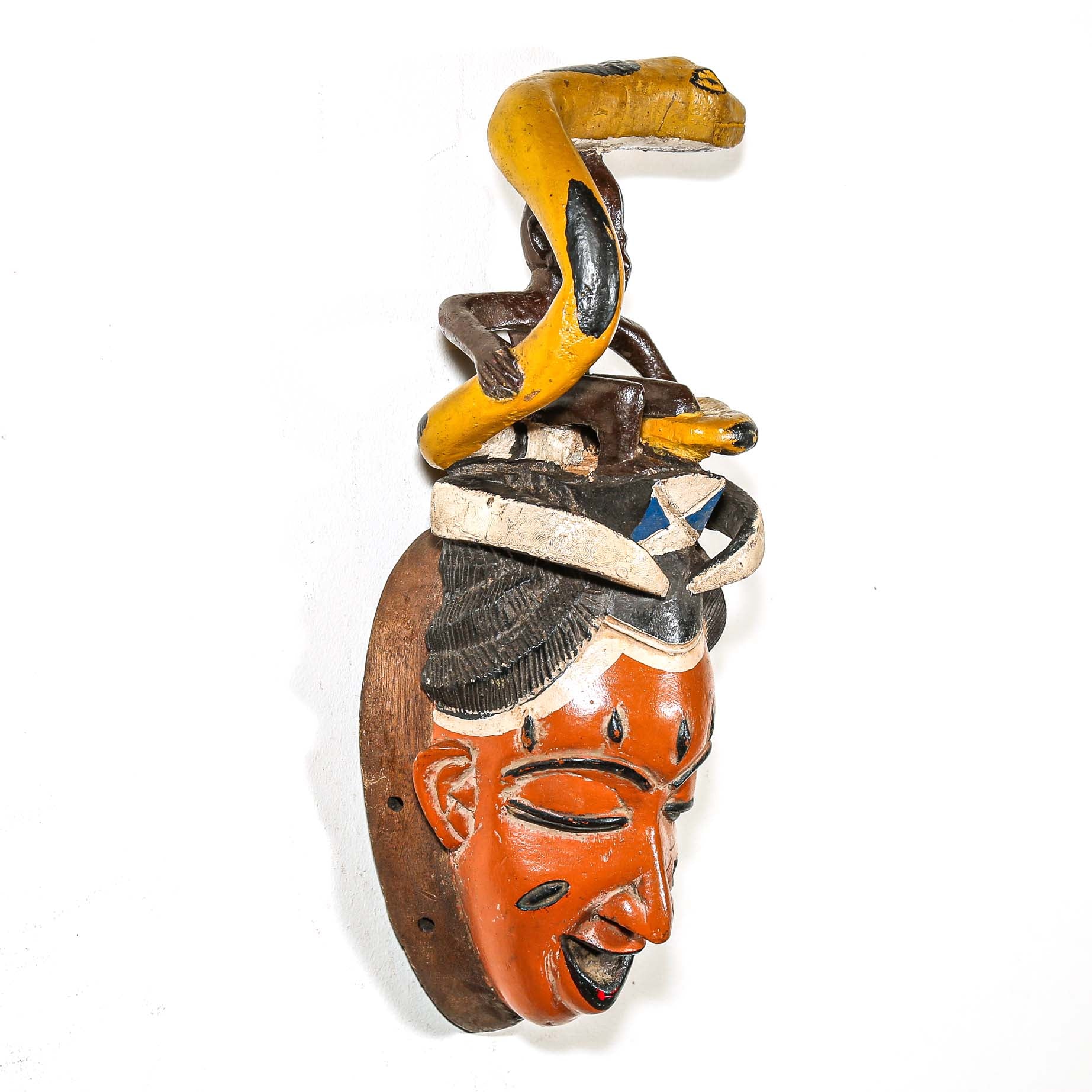 Carved wooden mask with a face and snake on a white background