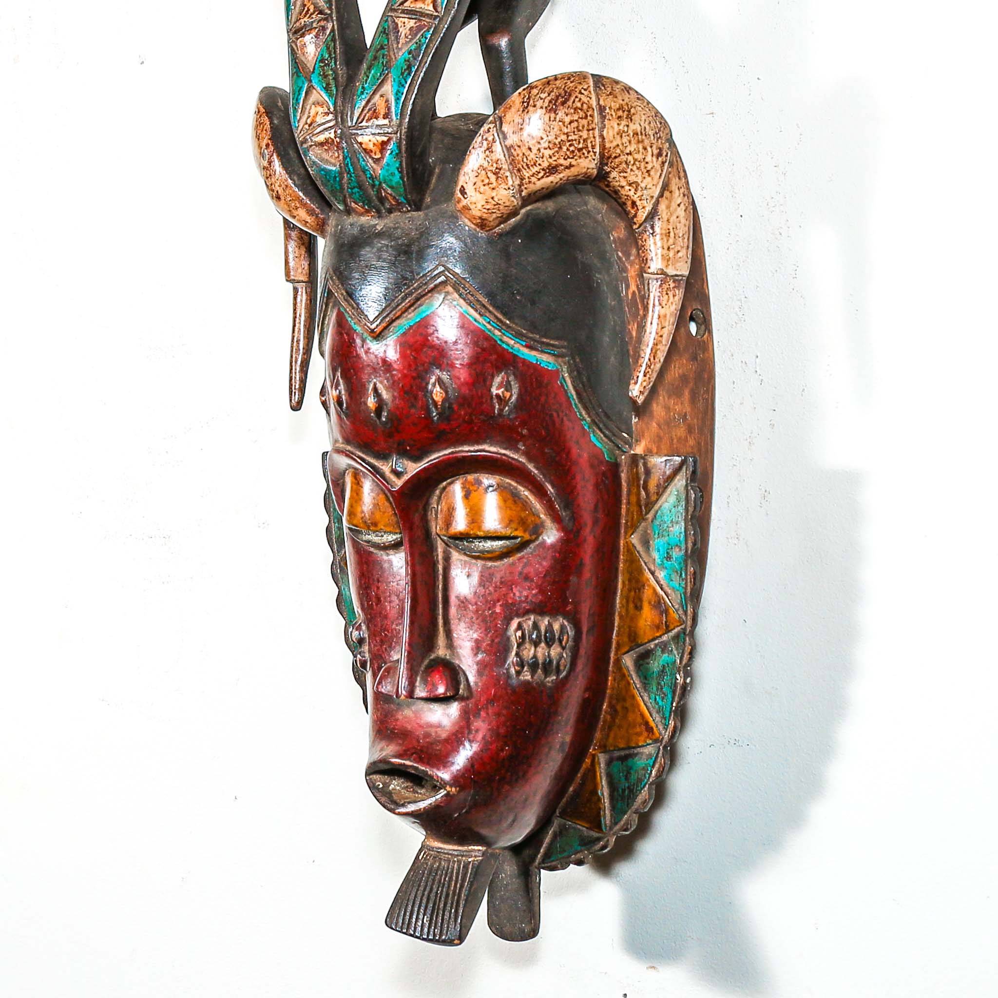 Decorative hand made wooden mask by an African artist with intricate designs on a white background