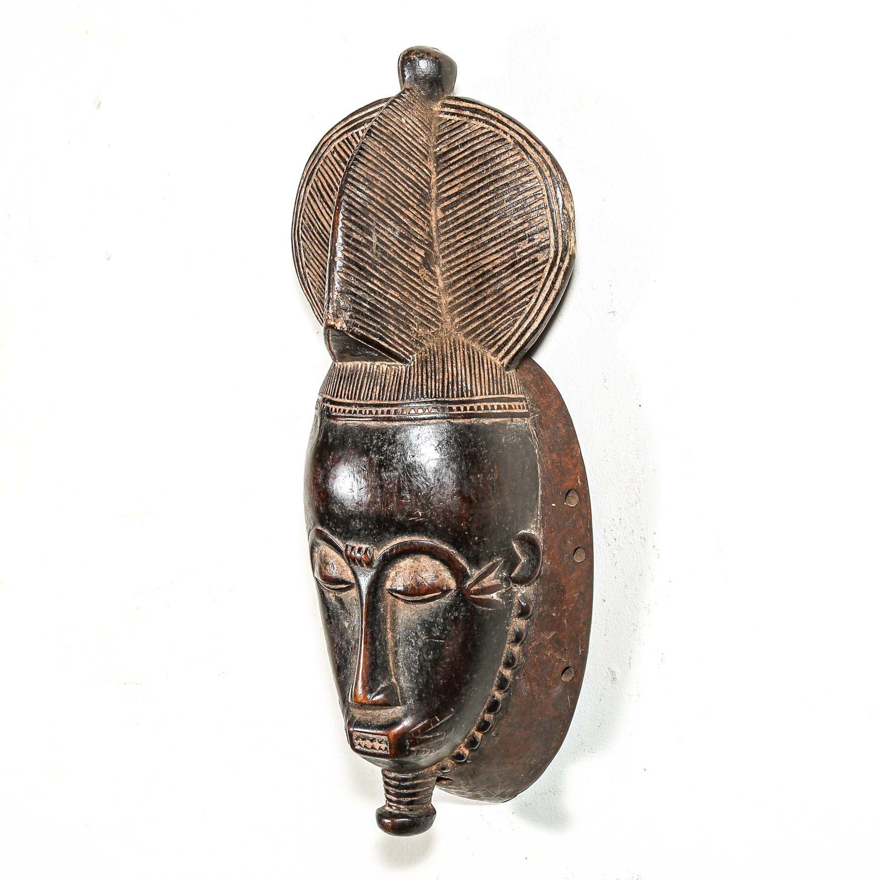 African black art mask made from wood with elaborate hair style hanging on a white wall