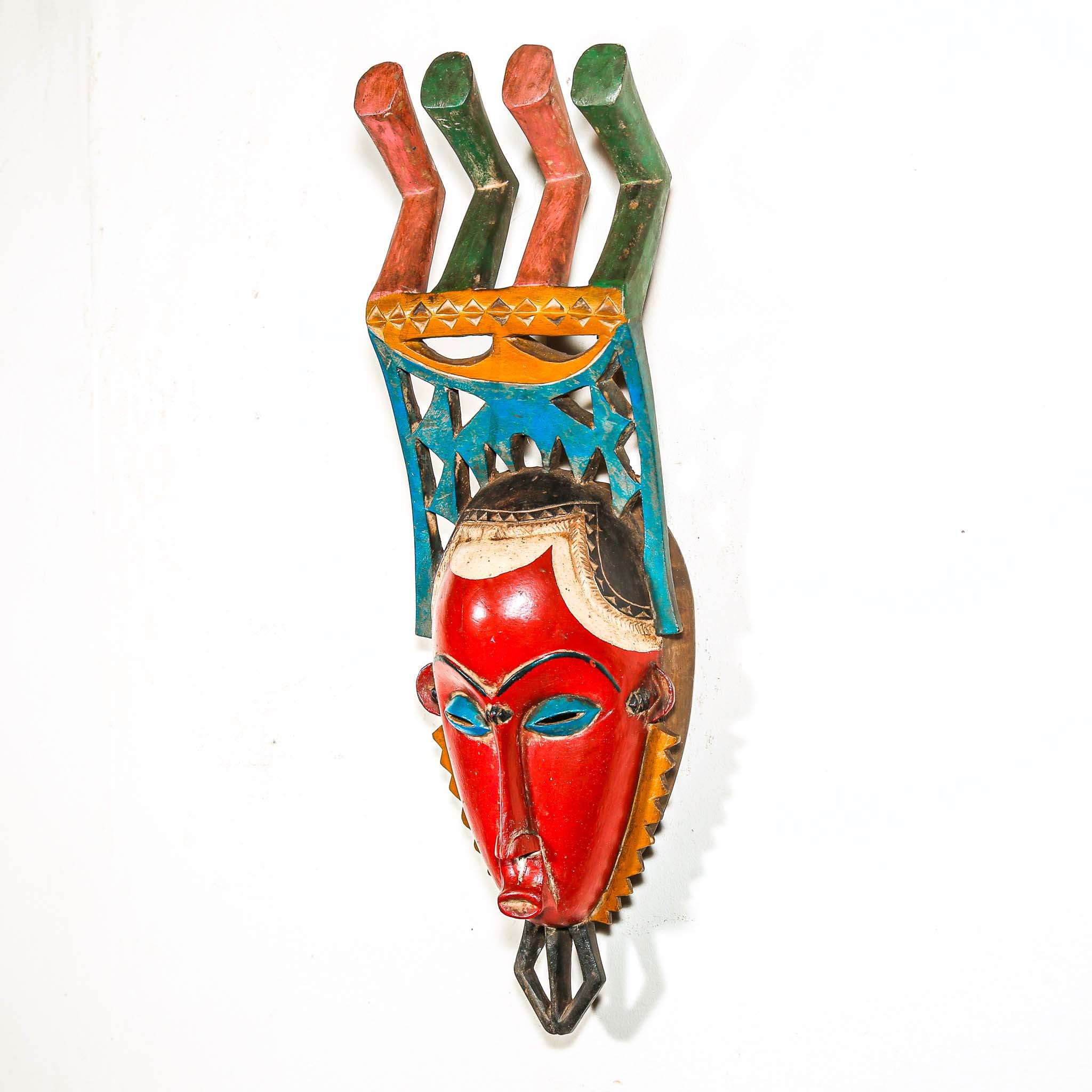 authentic tribal ceremonial red mask from Africa with colorful aesthetic displayed on a white wall