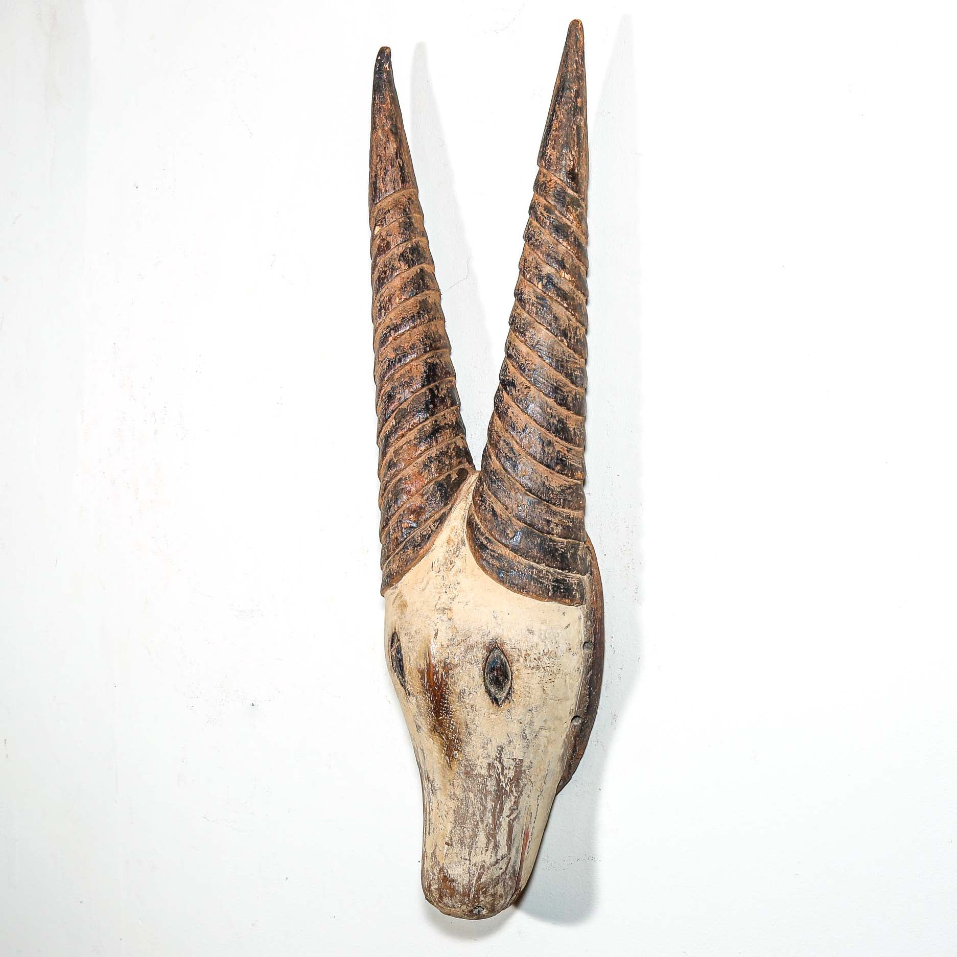 African mask in the shape of an antelope hanging on a white wall