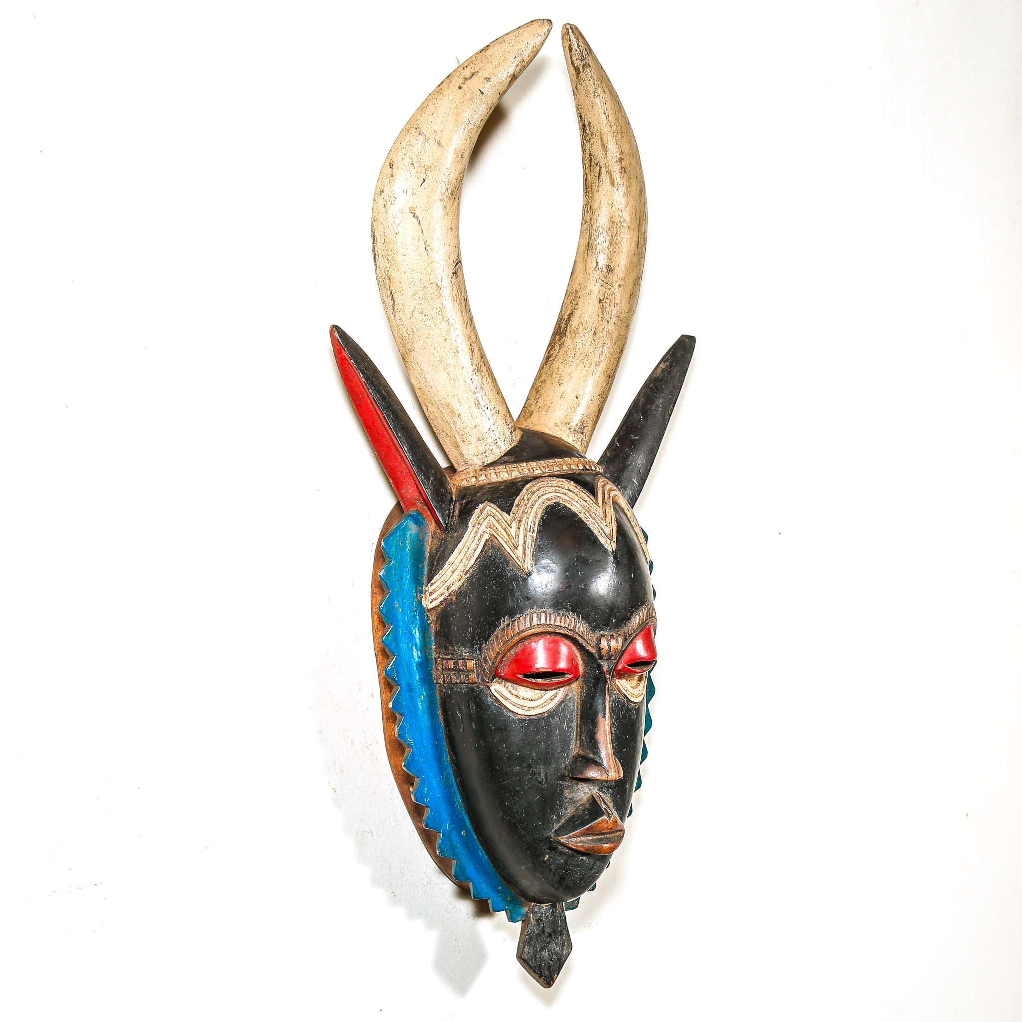 A vintage colorful African wood mask with large horns and a black face on a white background