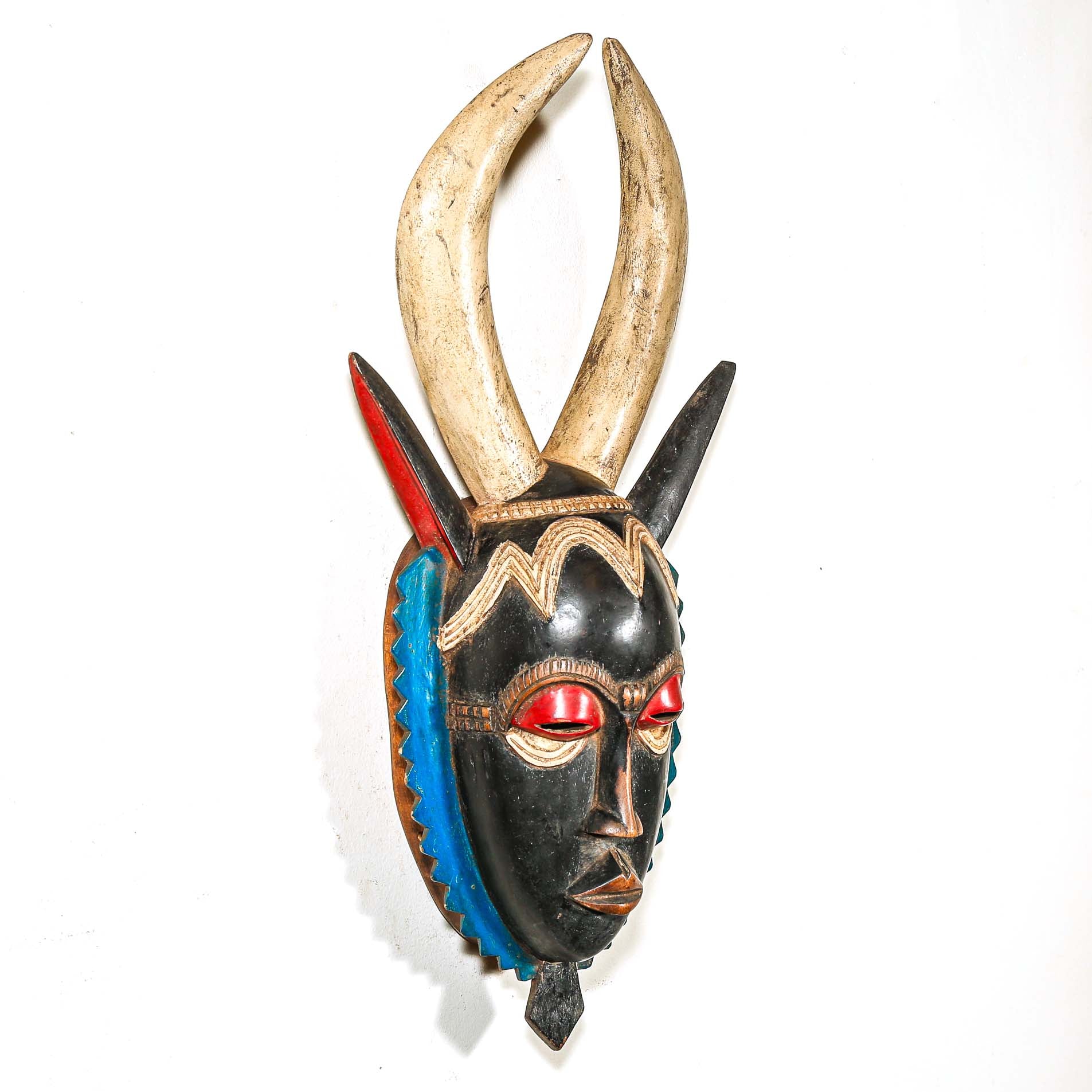 A vintage colorful African wood mask with large horns and a black face on a white background
