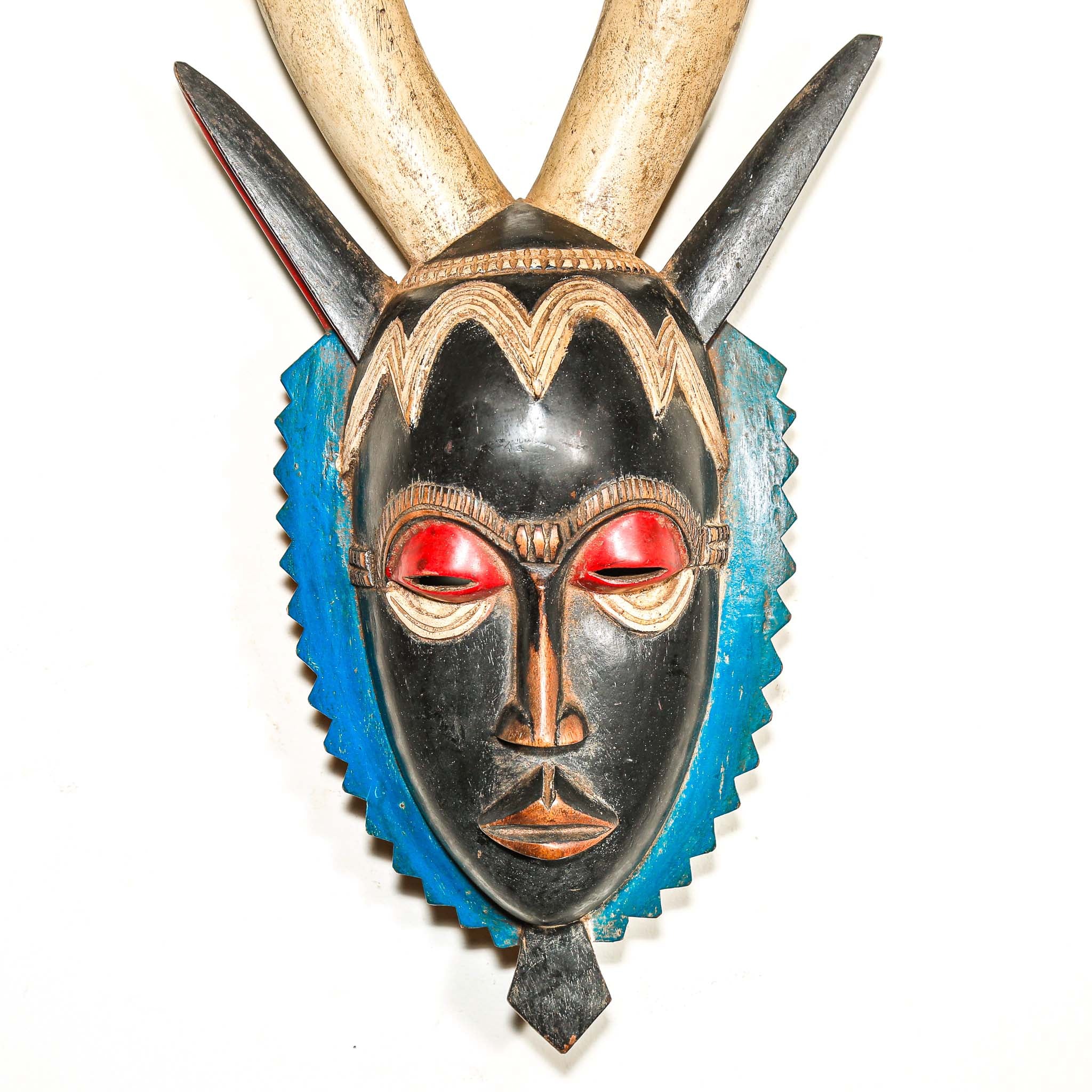 A vintage colorful African wood mask with large horns and a black face on a white background
