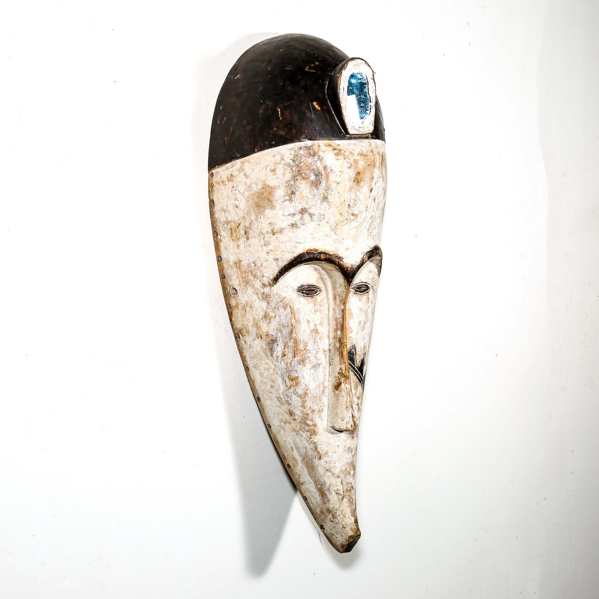 Authentic African mask to purchase online with neutral color designs hanging on a white wall