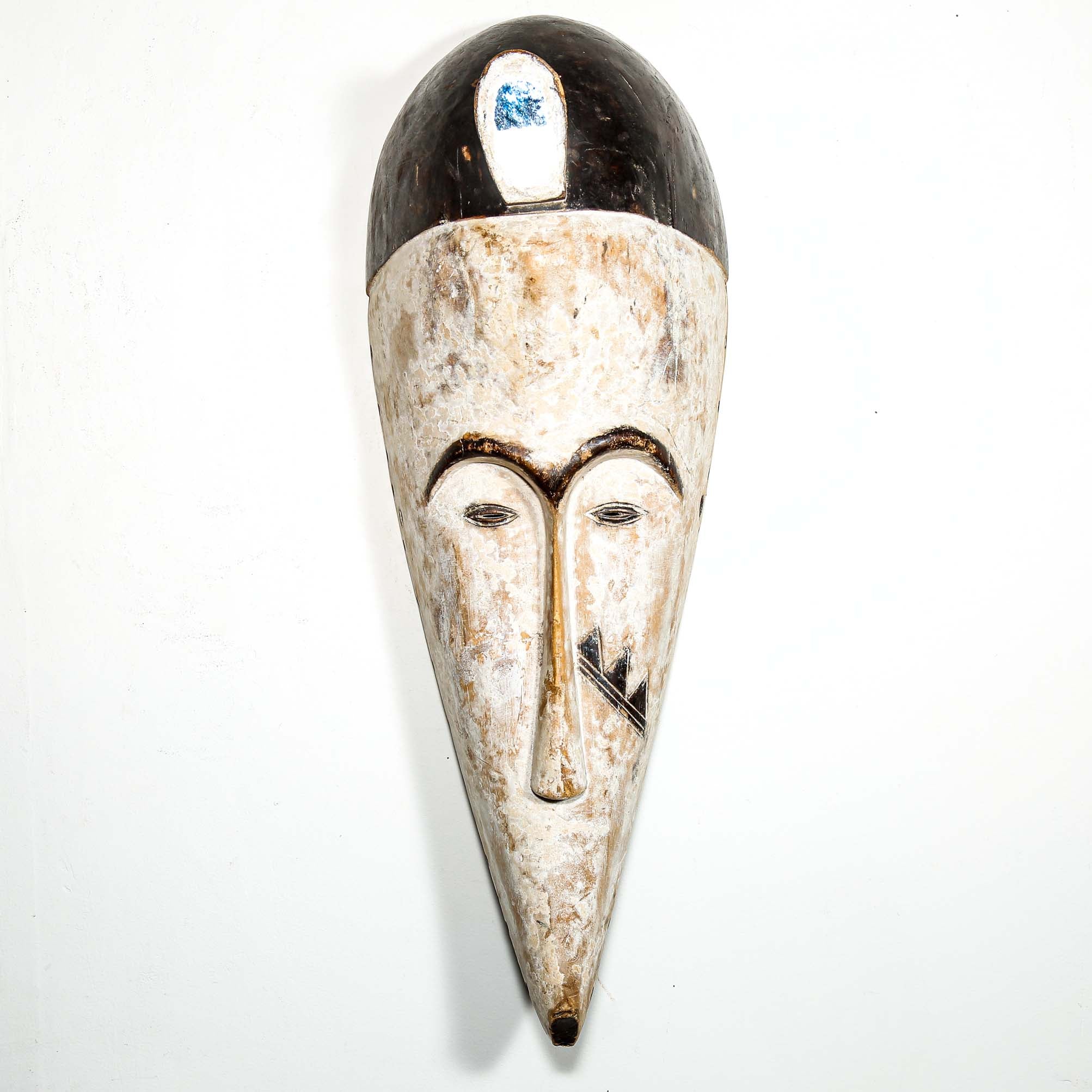 Authentic African mask to purchase online with neutral color designs hanging on a white wall