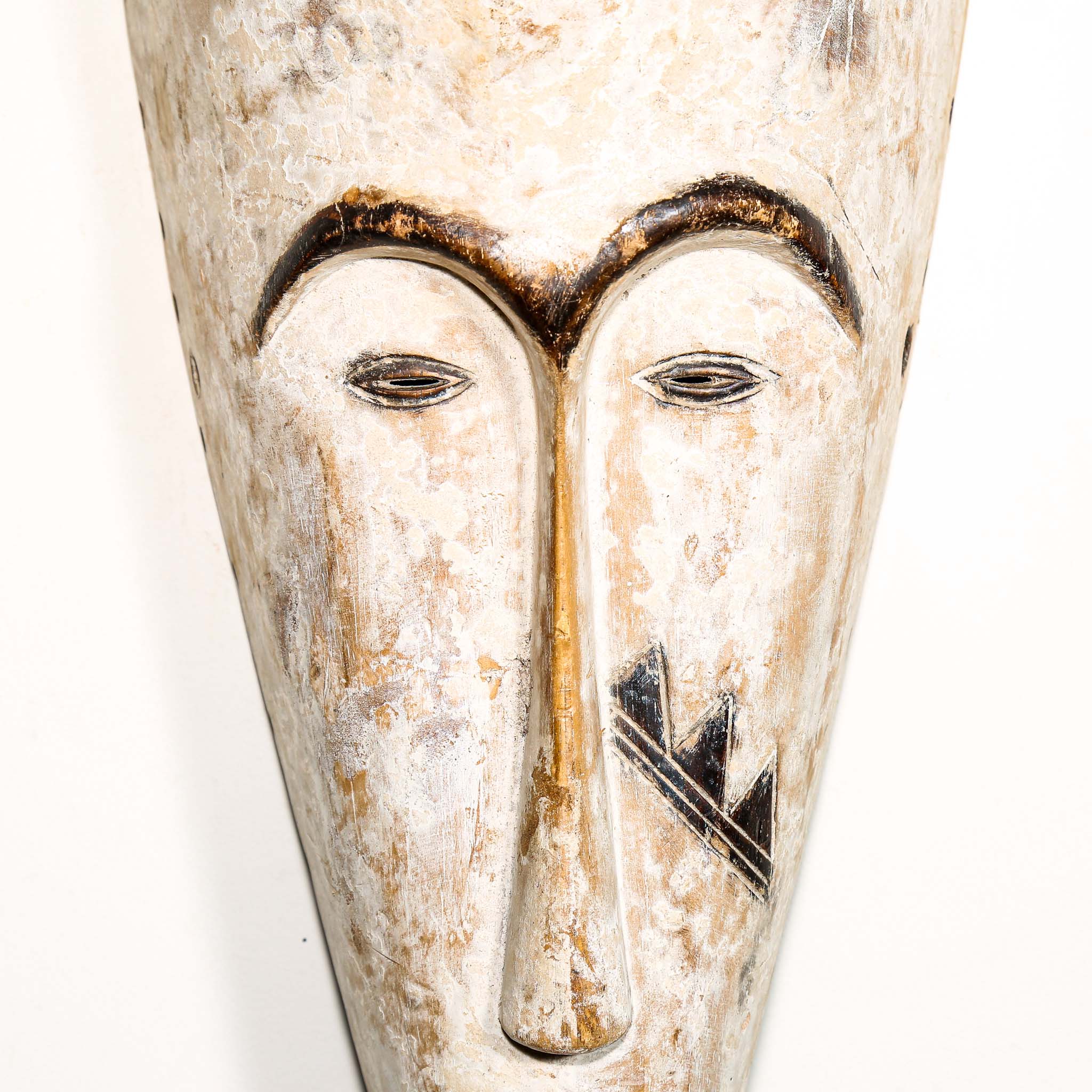 Authentic African mask to purchase online with neutral color designs hanging on a white wall
