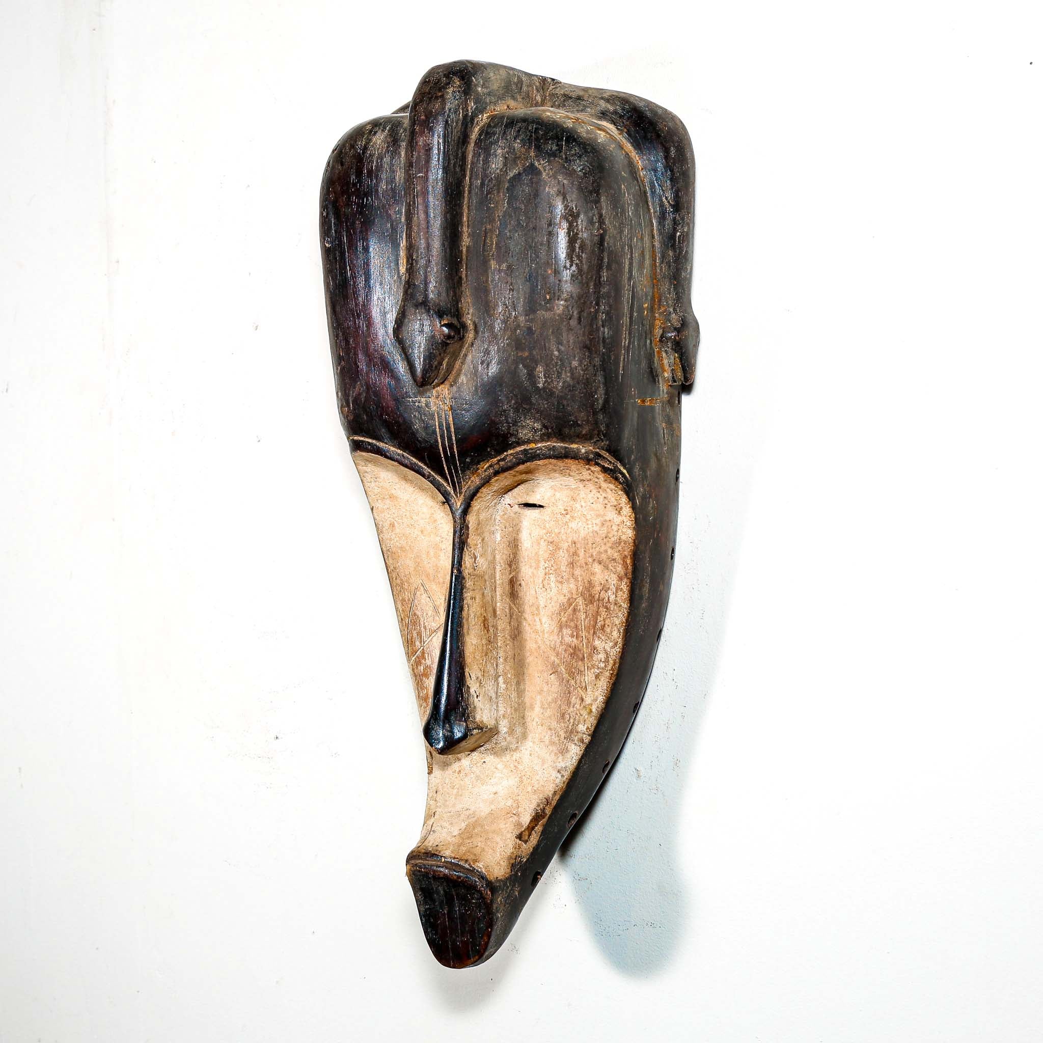 Authentic African mask to purchase online with neutral color designs hanging on a white wall
