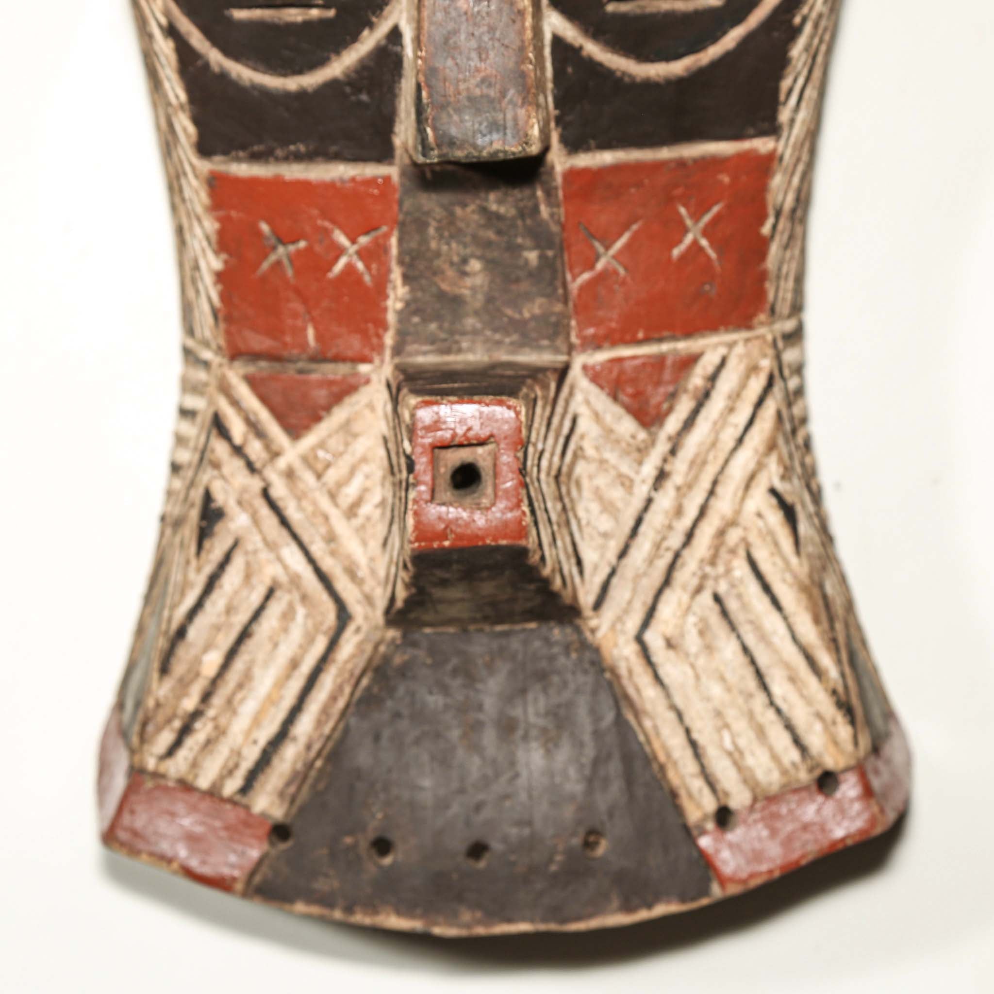 African art piece, specifically a wooden mask with geometric patterns on a white background. Tribal African art for sale.