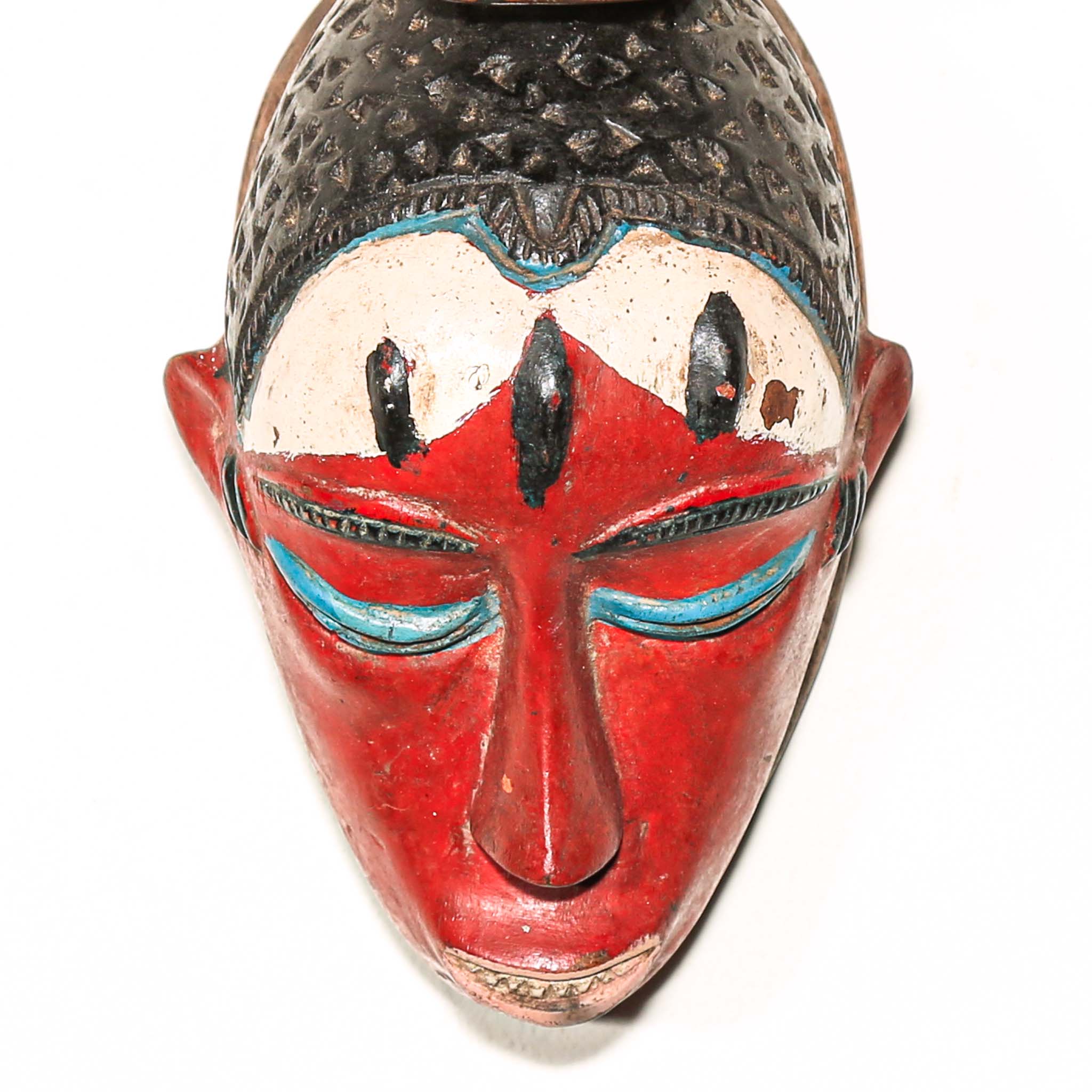 Colorful Decorative African mask with a small animal figure on top hanging on a white wall