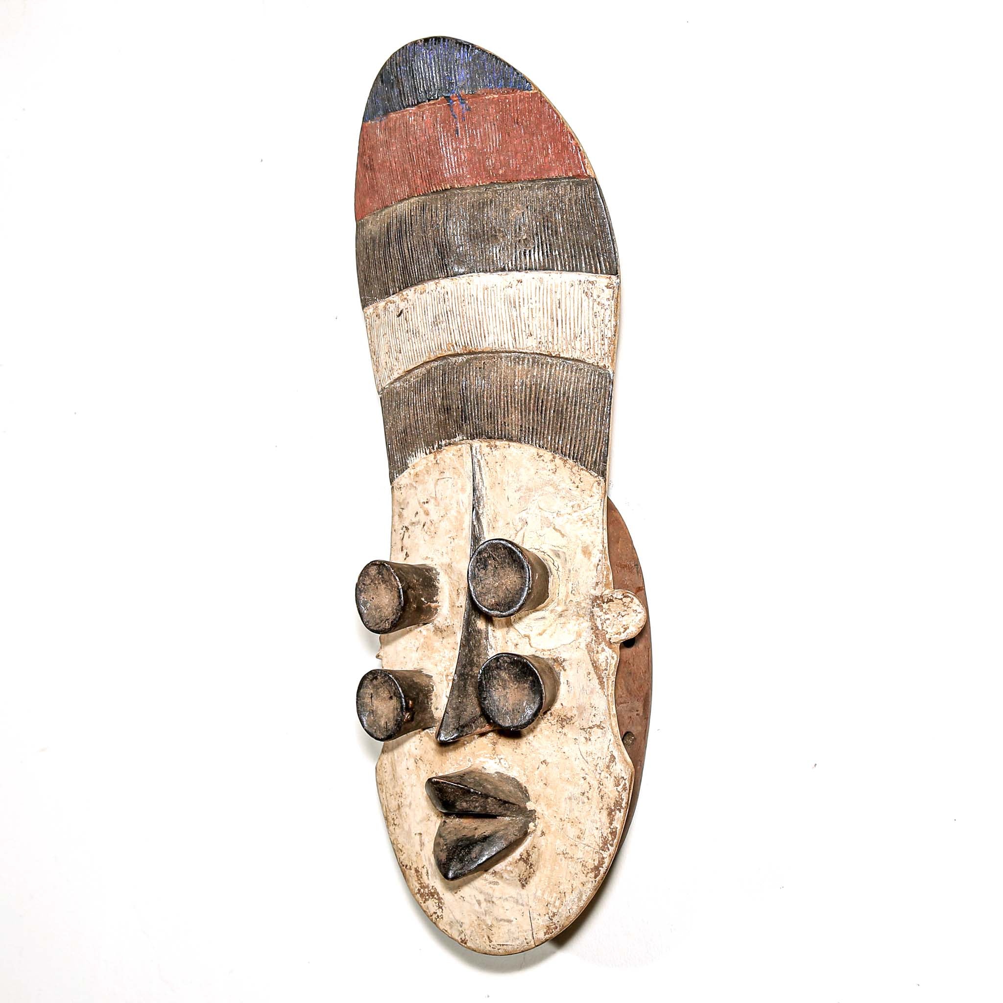 Wooden mask from Africa with striped patterns and four eyes on a white wall