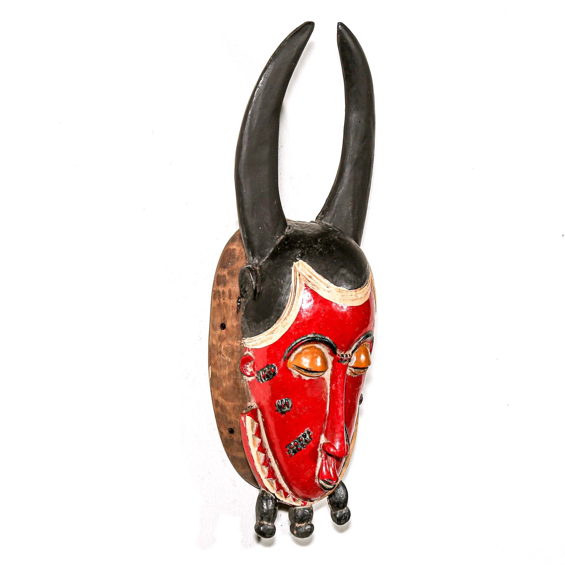 Red and black horned African mask on a white background