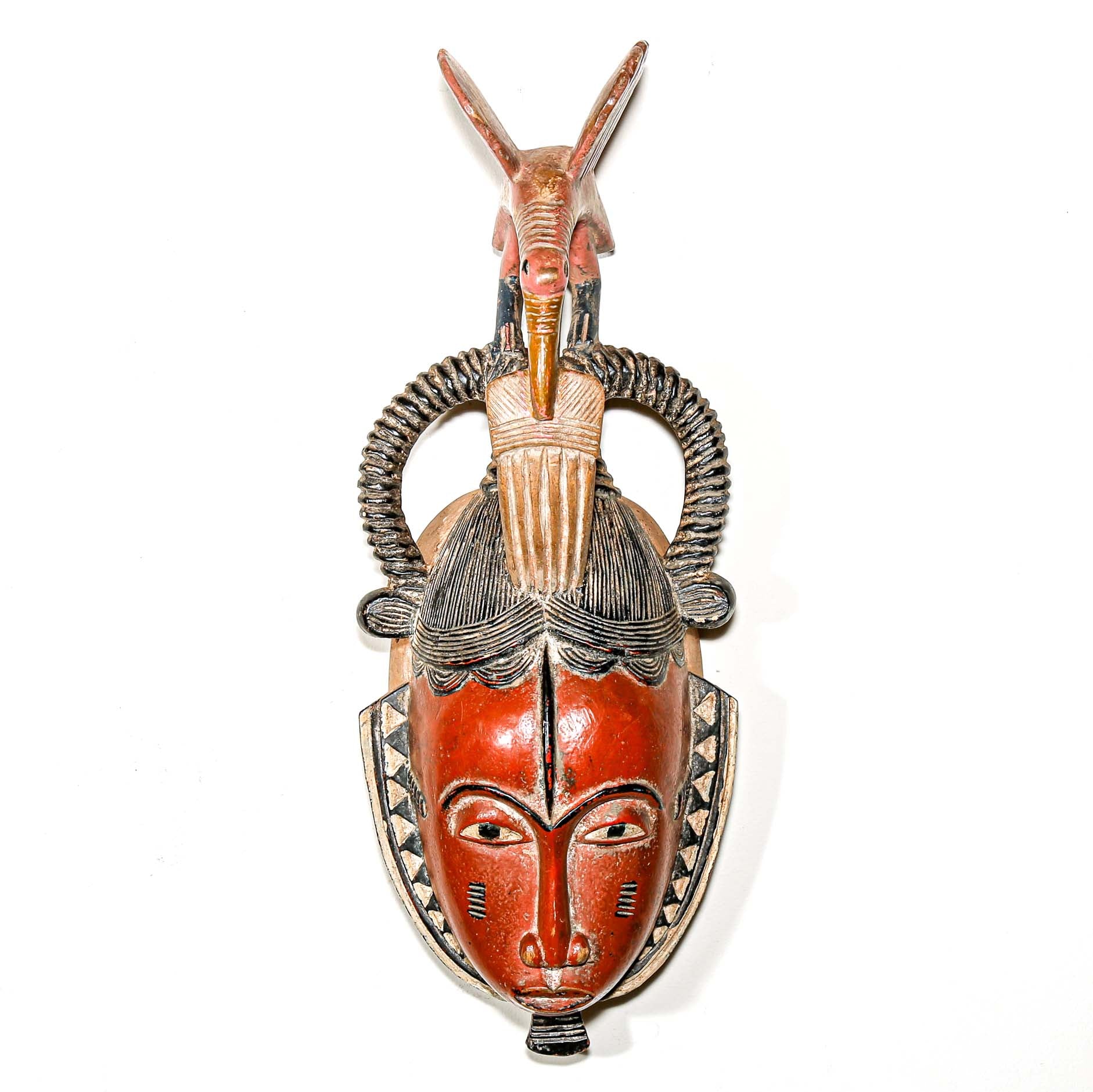 Colorful modern tribal art from African for sale. Guro ceremonial mask woth a carved bird hanging on a white wall