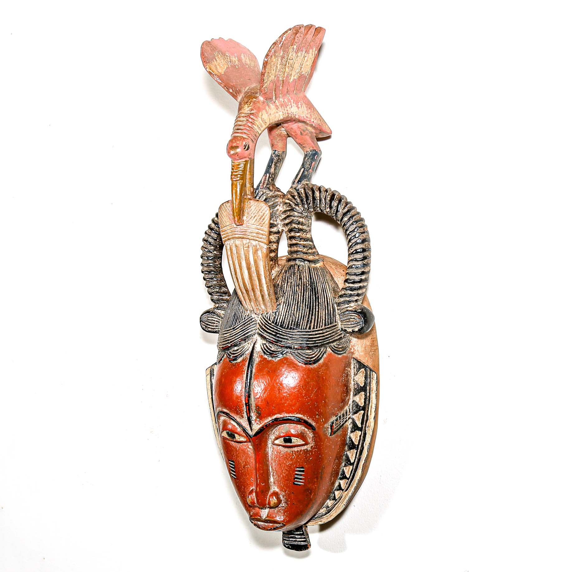 Colorful modern tribal art from African for sale. Guro ceremonial mask woth a carved bird hanging on a white wall