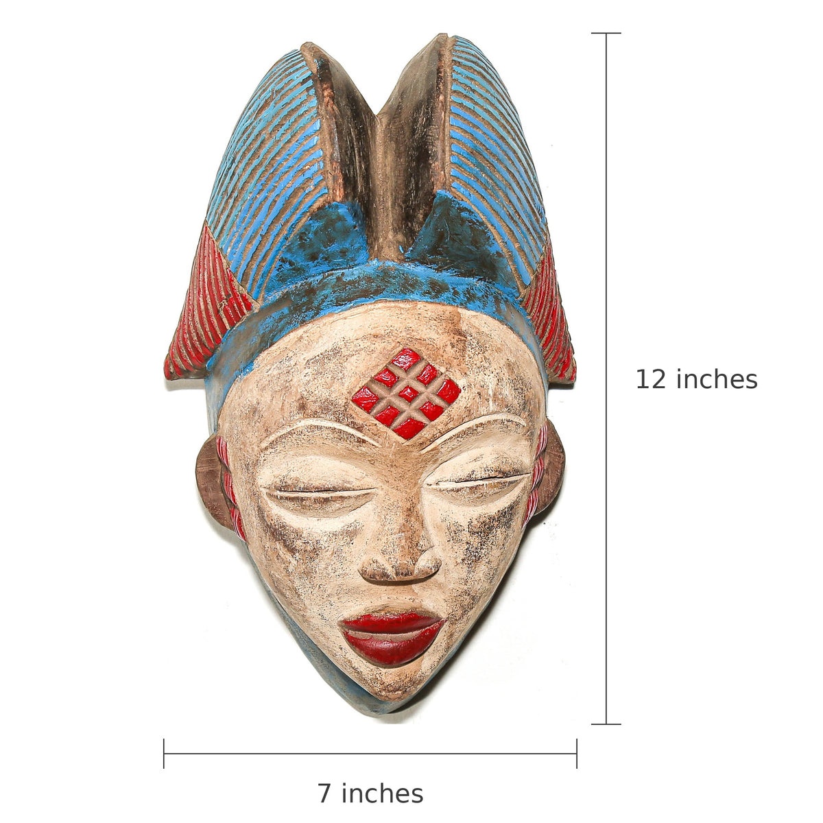 A carved decorative mask with a weathered beige face, red lips, a red diamond motif on the forehead, and a blue and red headdress, shown on a white background with dimension markers indicating 12 inches tall by 7 inches wide.