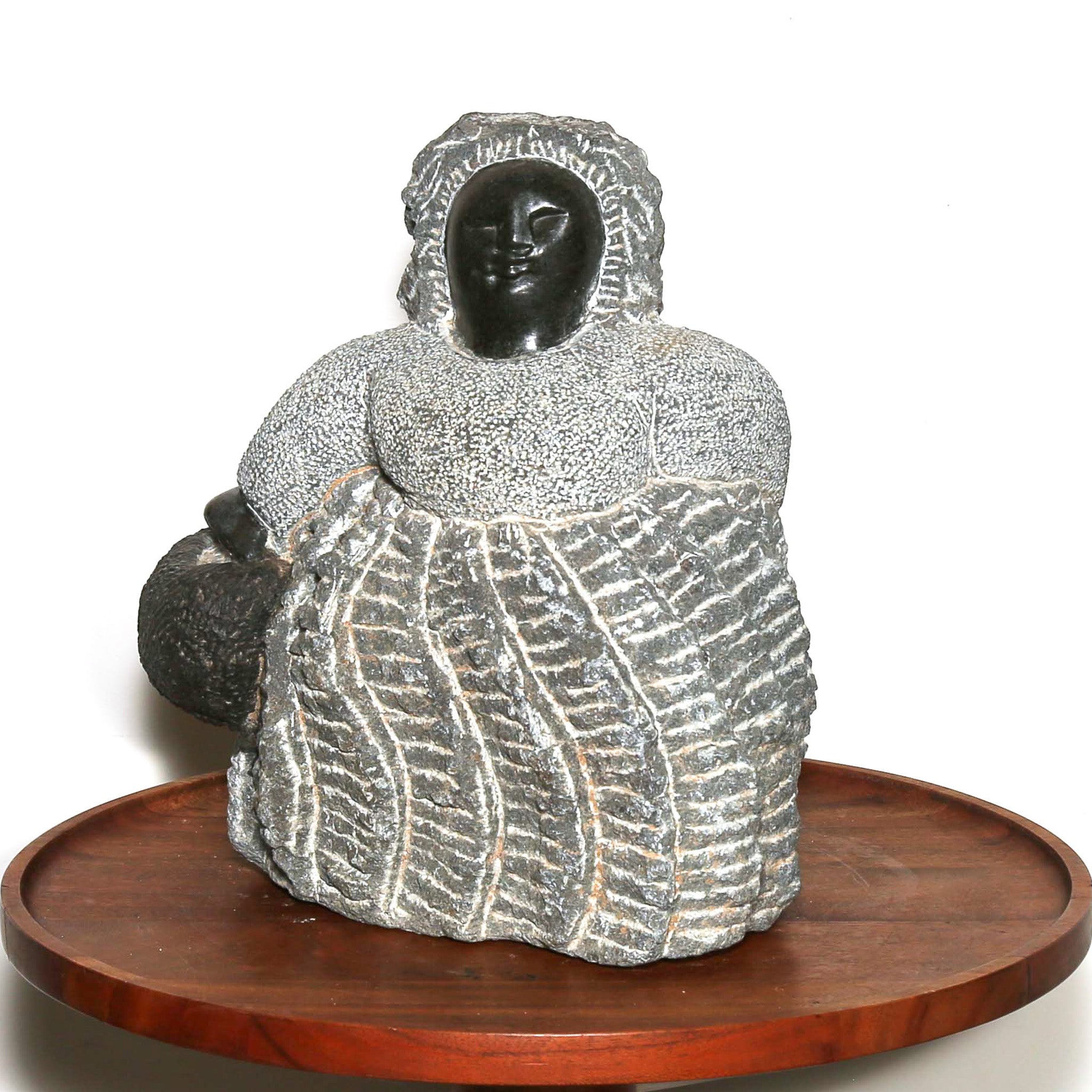 Sculpture of a woman holding a bag. Carved in rough grey stone. Made by hand in Africa.