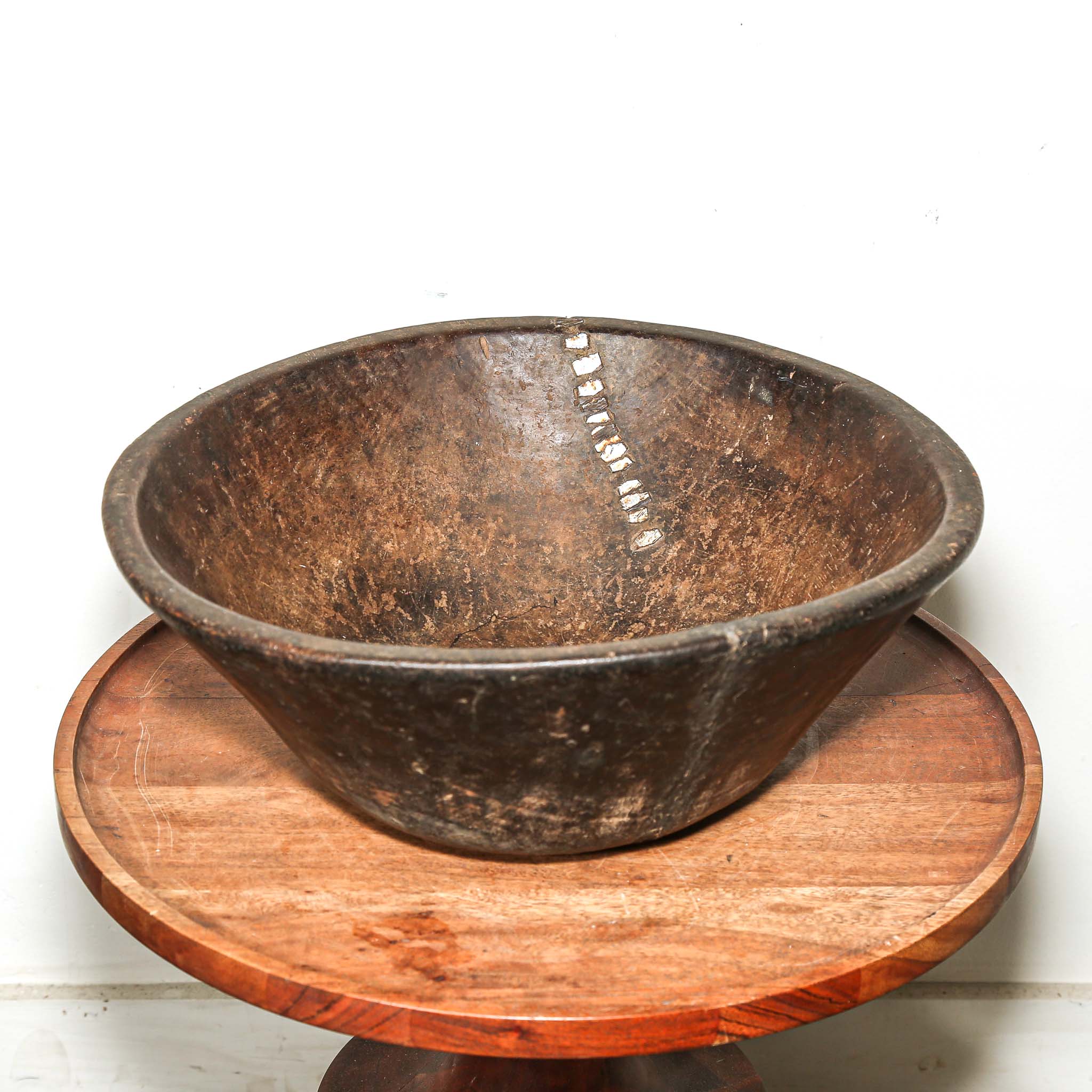 Rustic round Wooden bowl from vintage home decor from Africa on a wooden stand against a white background