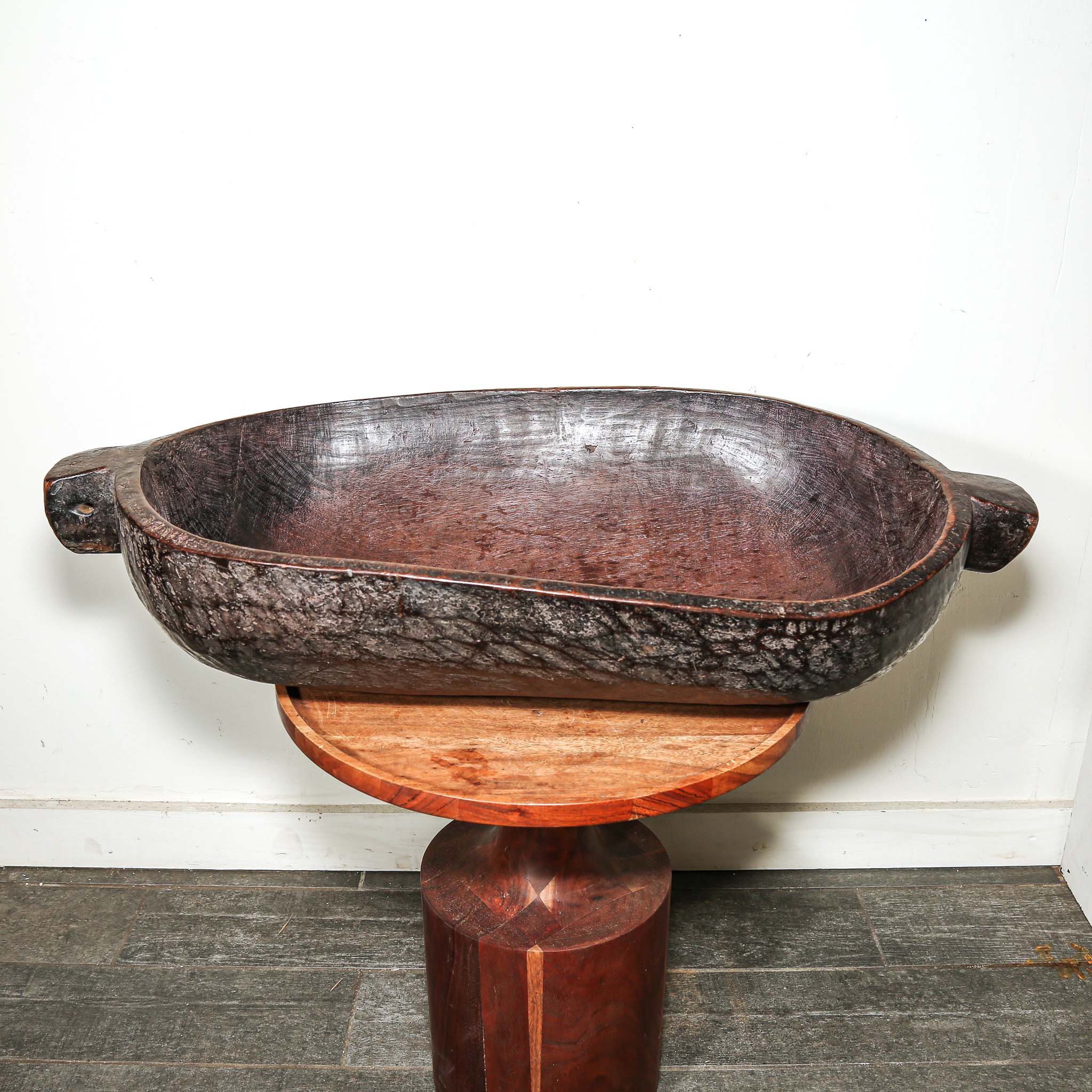 Decorative wooden vintage African oval bowl on a stand against a white wall
