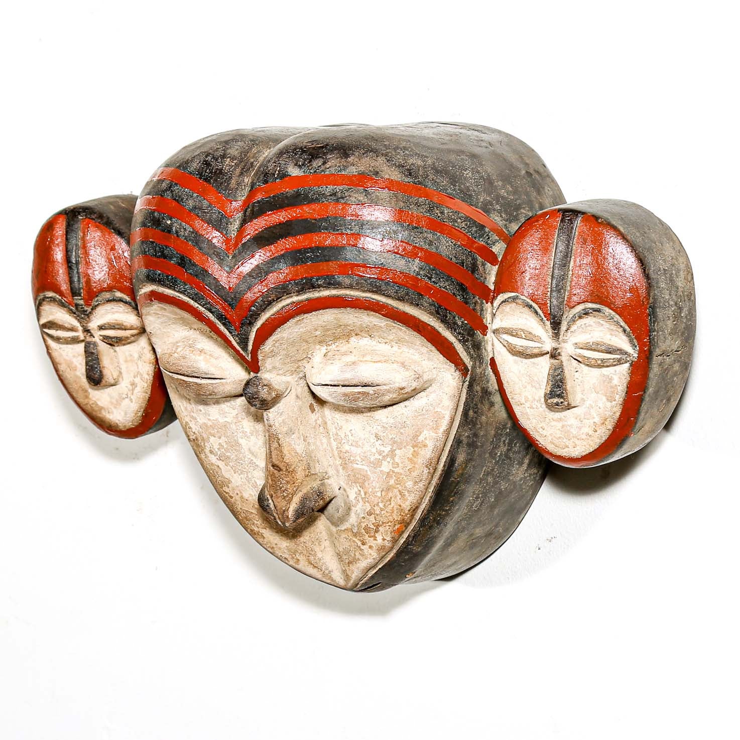 Carved stone mask with red and black patterns on a white background
