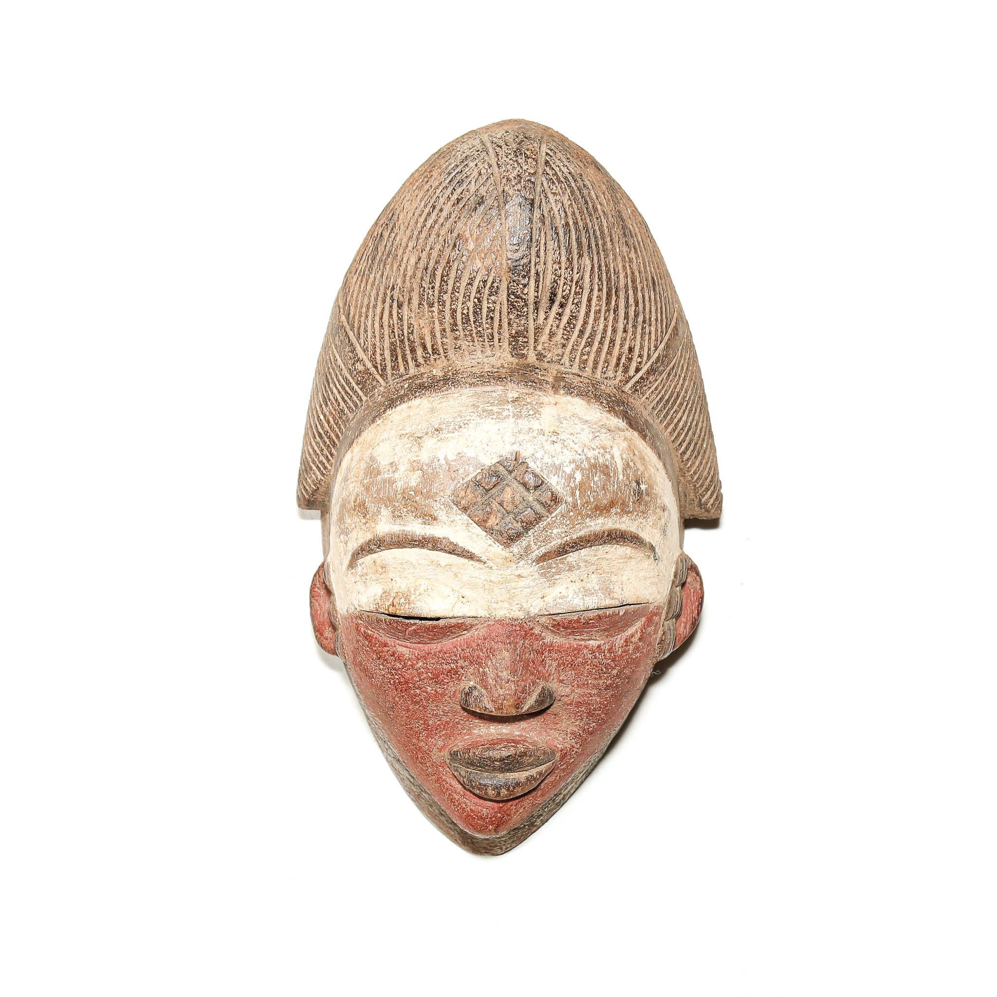 A carved wooden African-style mask with a tall textured hairpiece, featuring a painted face with a reddish-pink lower face, a white forehead with a diamond motif, and closed eyes, shown against a plain white background.