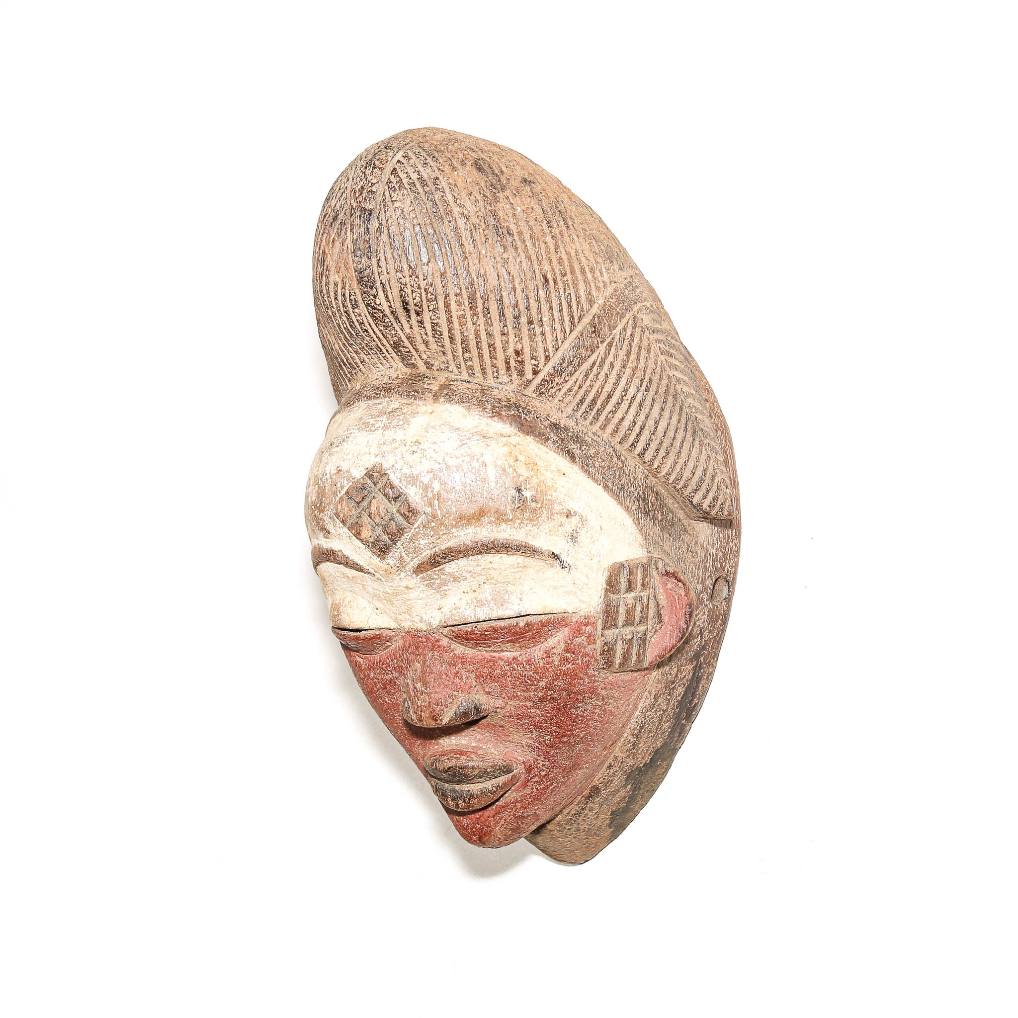 An African carved wooden mask depicting a woman with a high hairstyle, painted with terracotta red on the cheeks and a beige face, set against a plain white background.