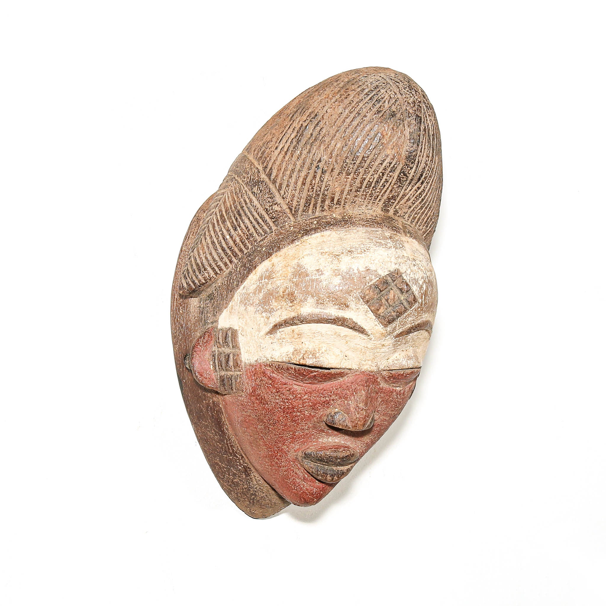 An African carved wooden mask depicting a woman with a stylized hairstyle, painted with beige and reddish-brown tones on a white background.