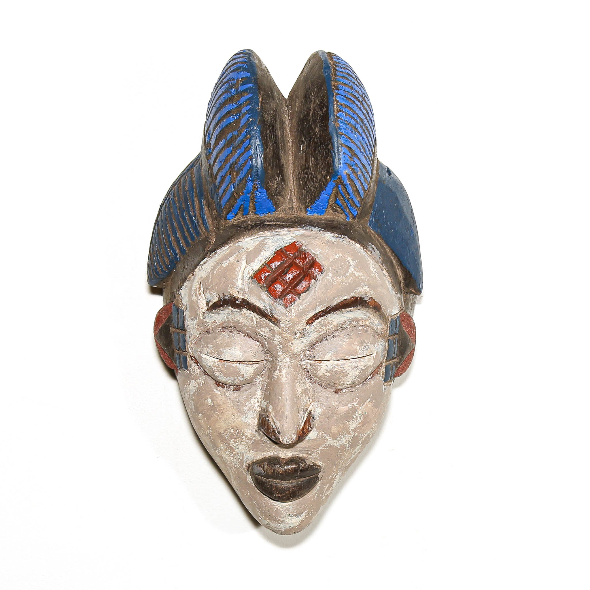 A carved African-style mask depicting a woman with closed eyes, a red geometric forehead design, and a blue and brown headdress, shown against a plain white background.