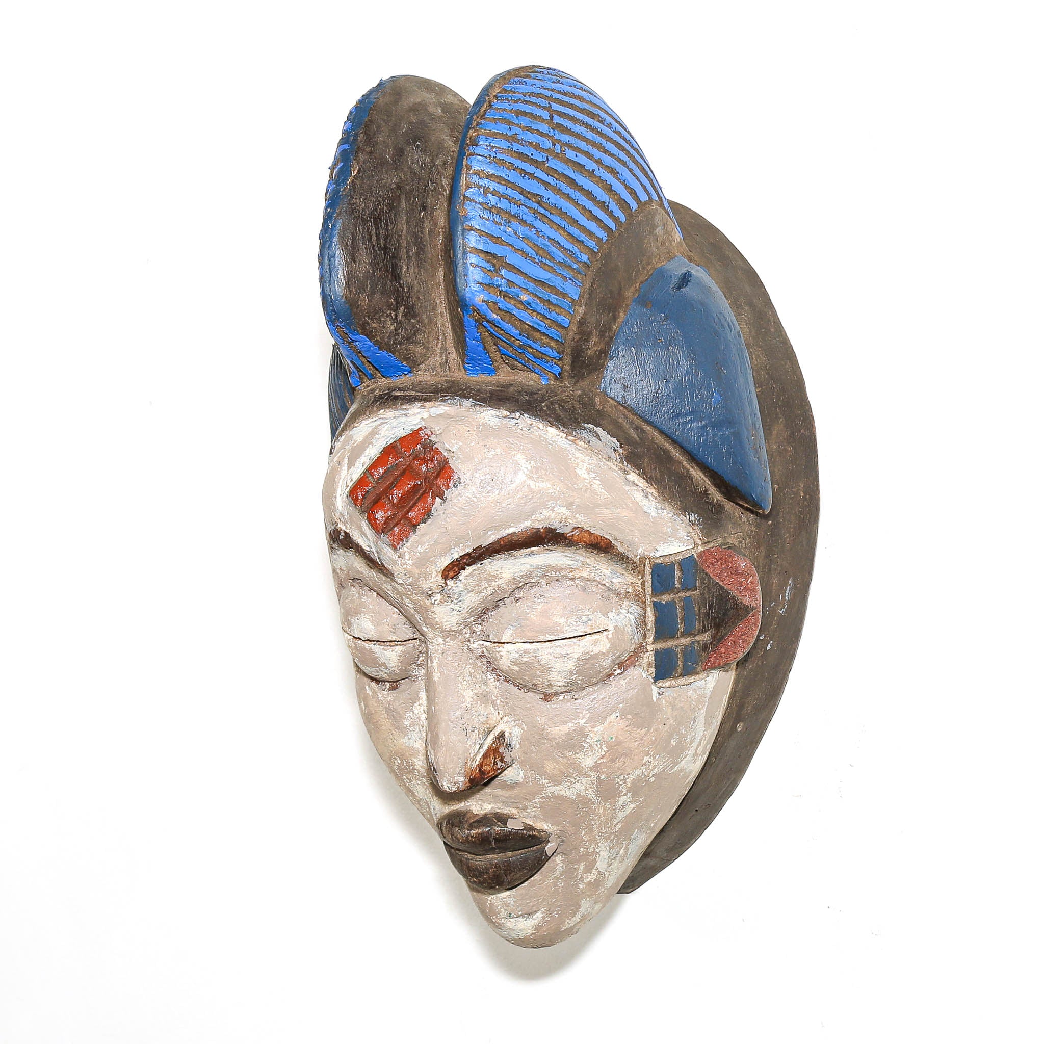 A hand-carved African wooden mask with a serene face, featuring blue and red painted details and a dark brown textured background, set against a plain white backdrop.