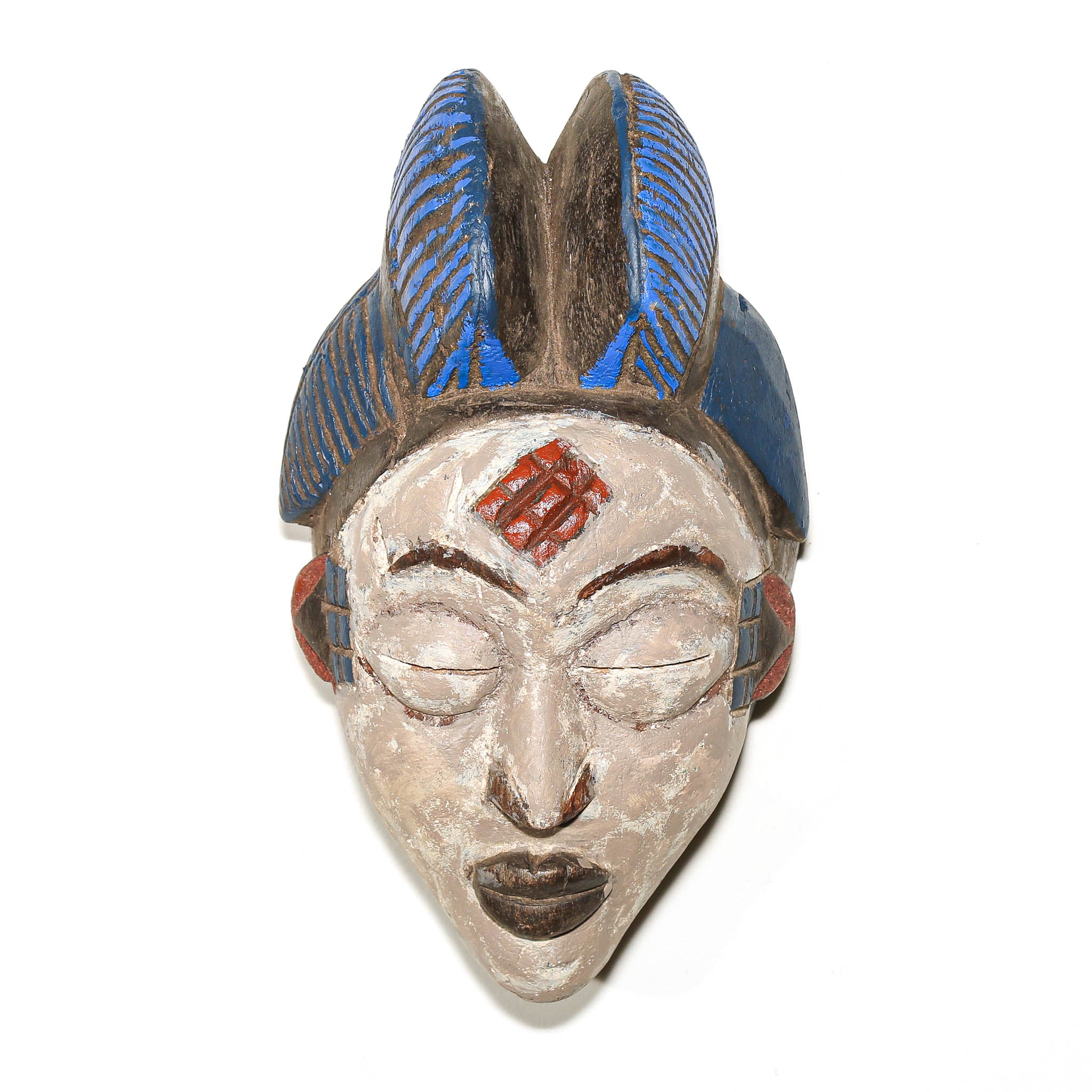 A carved African-style wooden mask with closed eyes, a red geometric forehead design, and a tall blue feather-like headdress, shown against a plain white background.