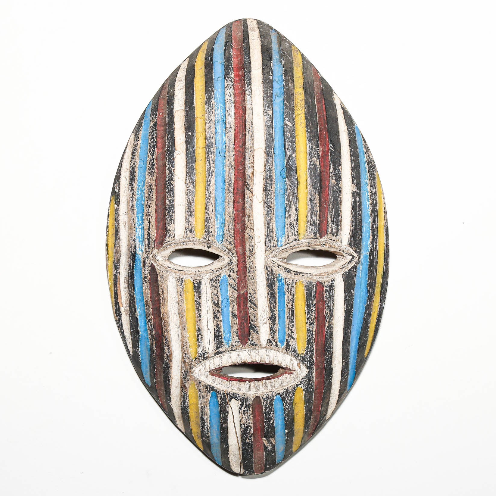 A handcrafted wooden mask with a vertically striped pattern in blue, yellow, red, brown, black, and white, featuring cutouts for the eyes and mouth, shown against a plain white background.