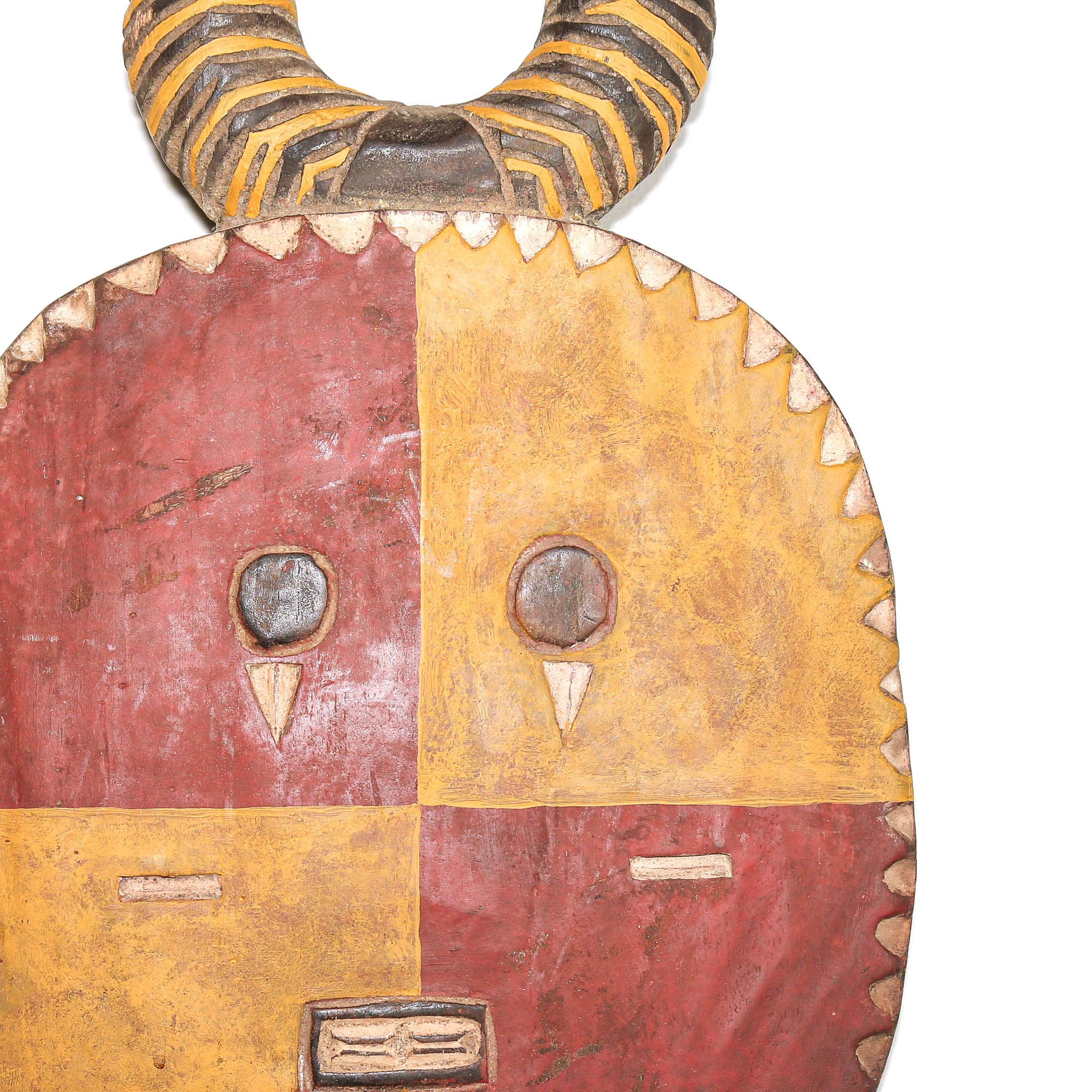 A hand-painted wooden African-style mask with a curved horn, featuring a four-quadrant face in red and ochre yellow with carved eye sockets and triangular nose details, isolated on a white background.