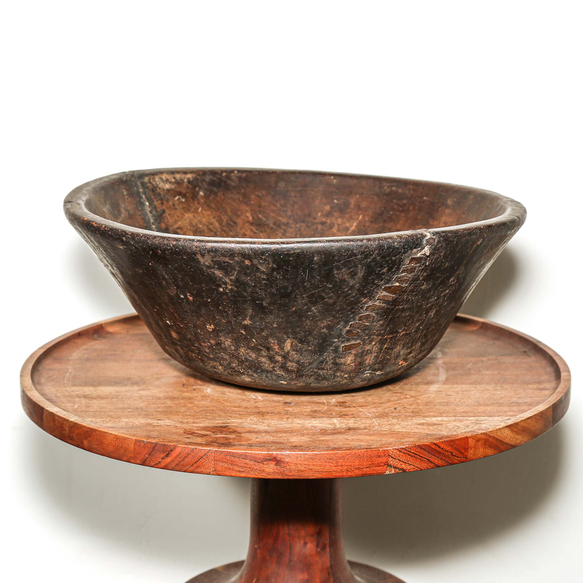 Rustic round Wooden bowl from Africa on a wooden stand against a white background