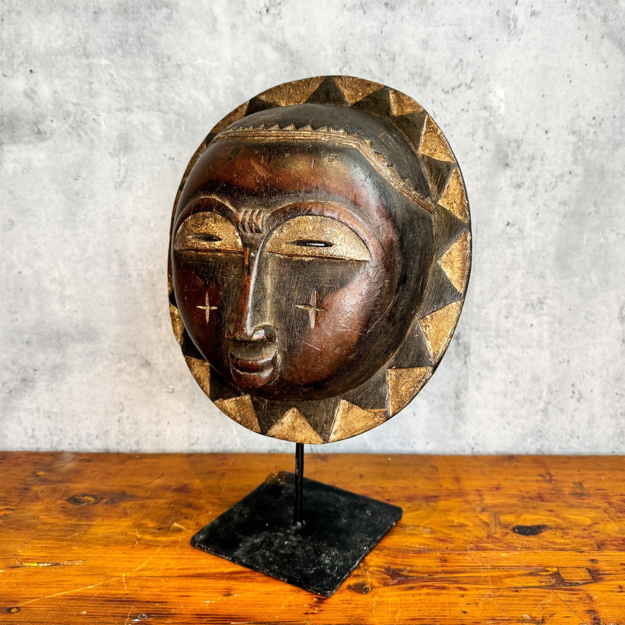 Baule Sun Mask from Cote d'Ivoire displayed on a stand as an African mask skewed to the left