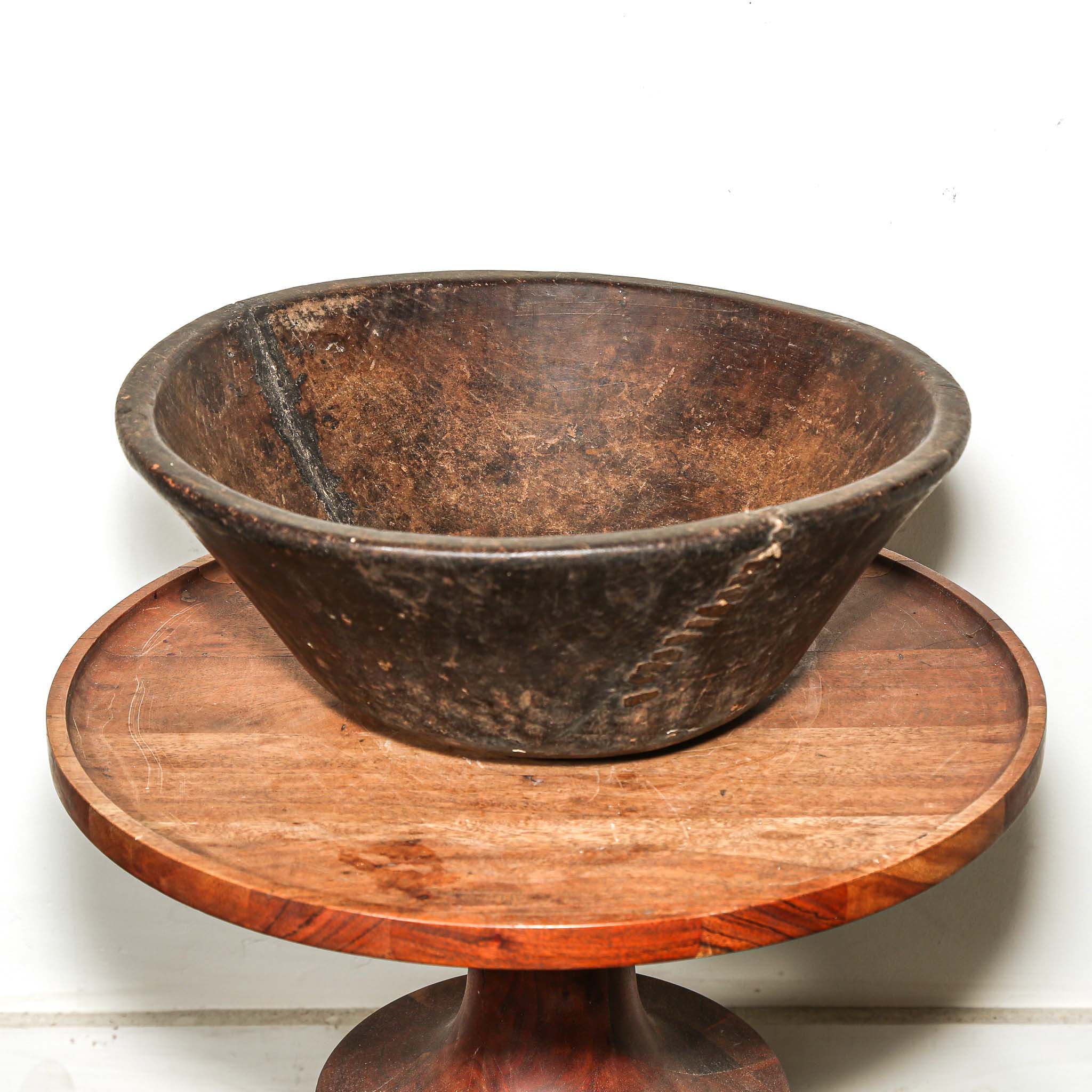 Rustic round Wooden bowl from vintage home decor from Africa on a wooden stand against a white background