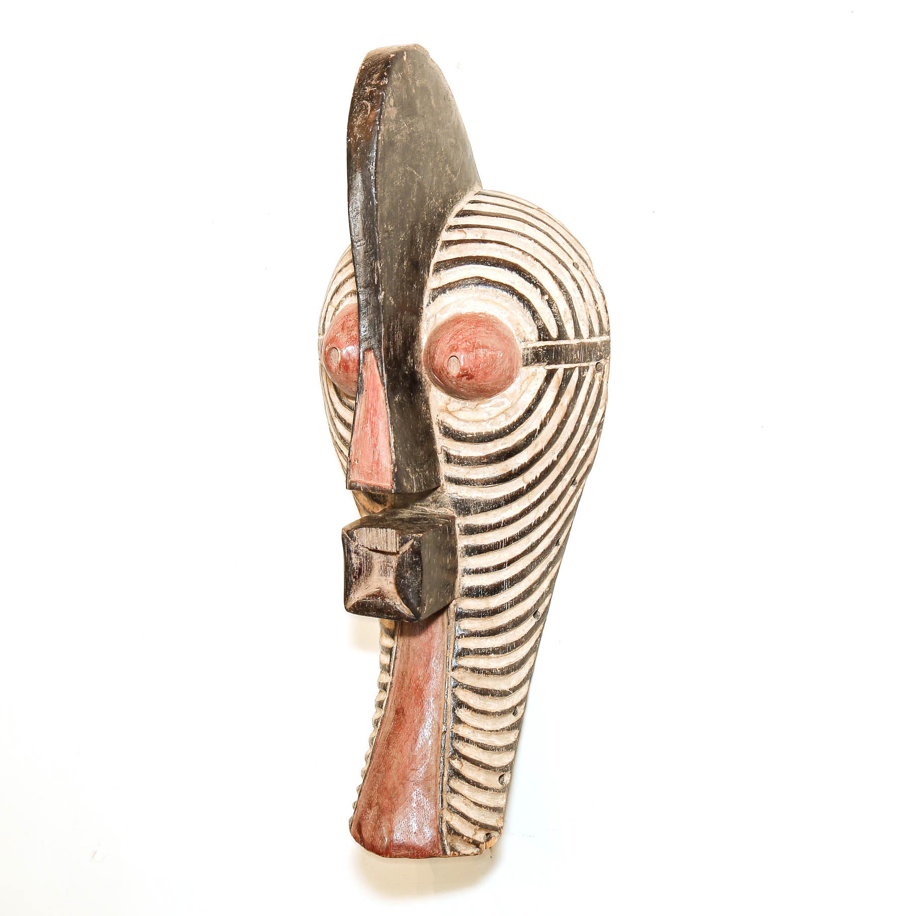 A hand-carved African wooden mask with a stylized face, featuring black, white, and reddish-pink painted details, set against a plain white background.