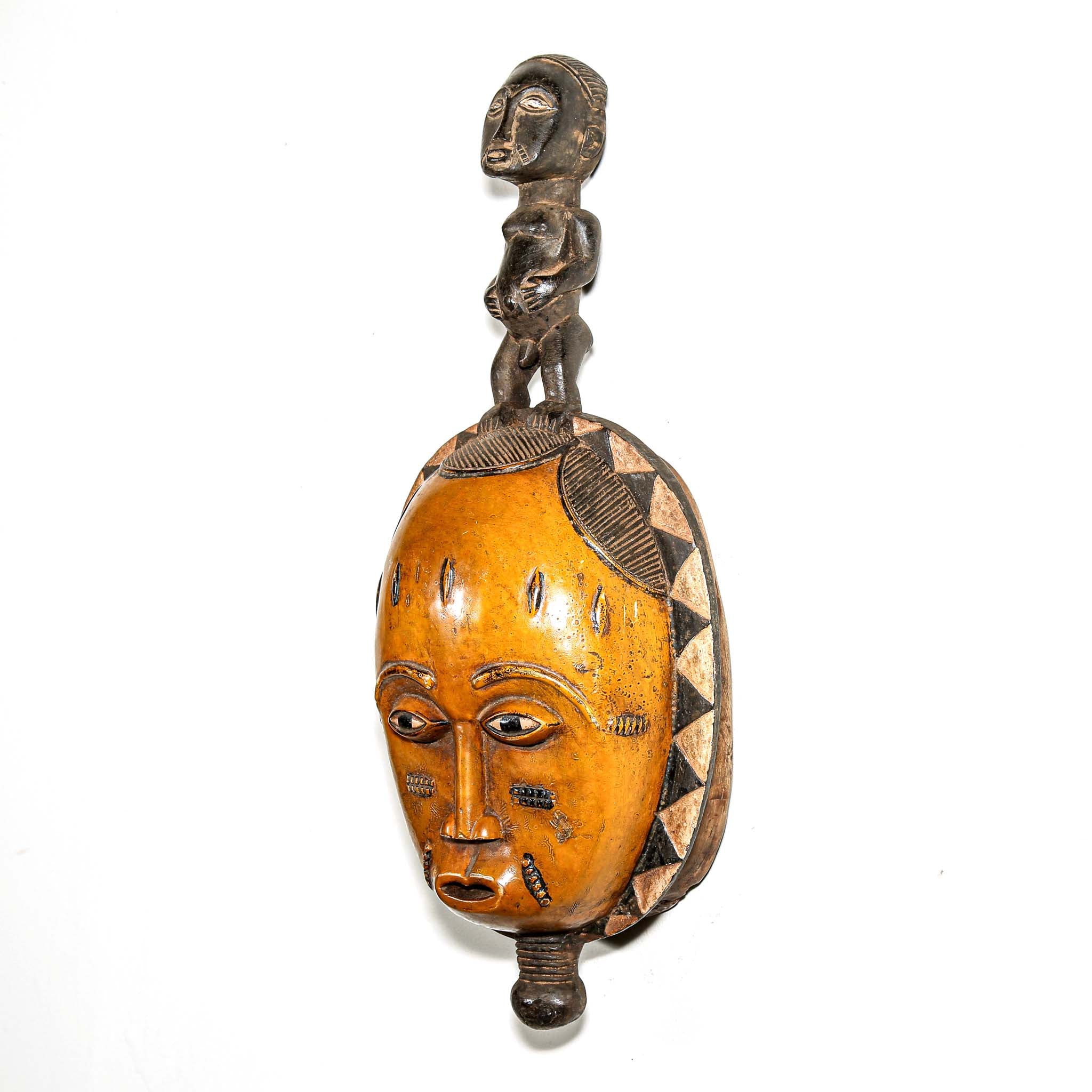 African mask with a carved wooden yellow face and figure on the head hanging on a white bedroom wall