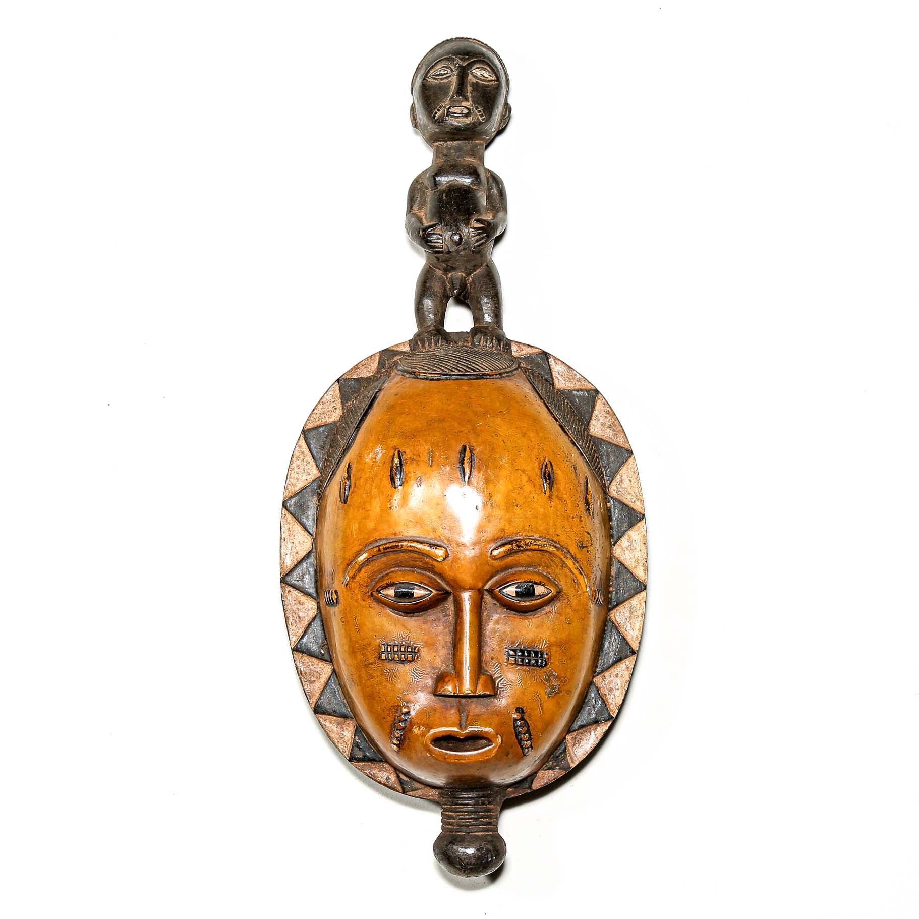 African mask with a carved wooden yellow face and figure on the head hanging on a white bedroom wall